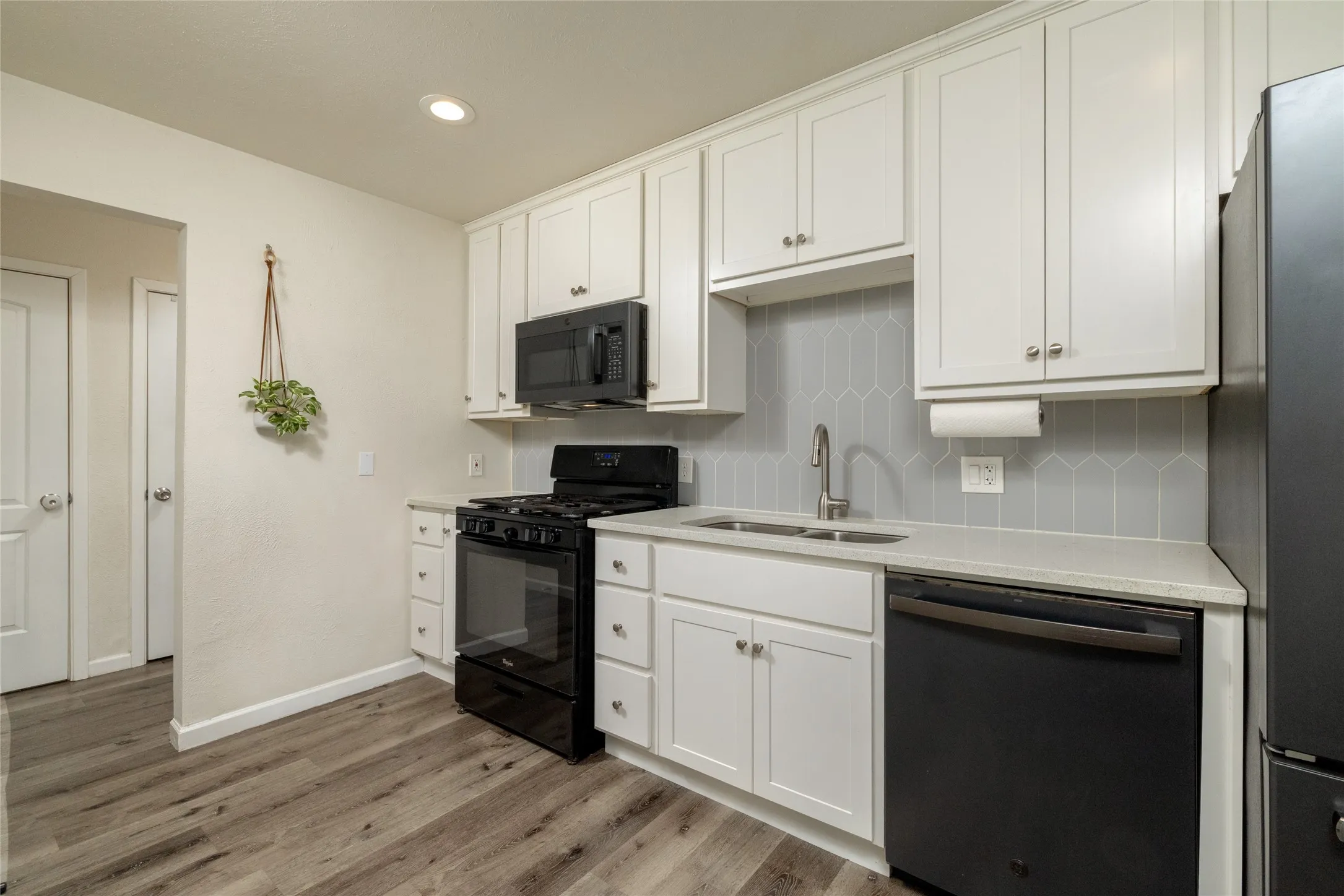 White cabinetry, light countertop, gray geometric tile backsplash, stainless steel sink with a gooseneck faucet, and wood-finish flooring