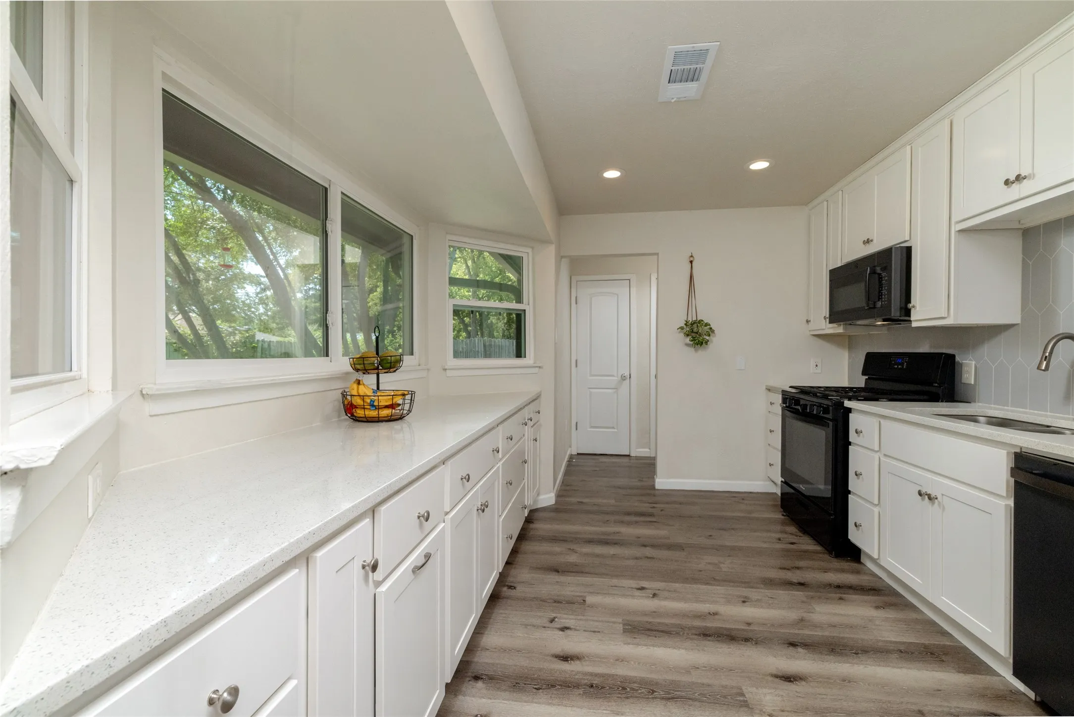 Kitchen featuring white cabinetry, light-toned countertops, wood-finish flooring, and black appliances