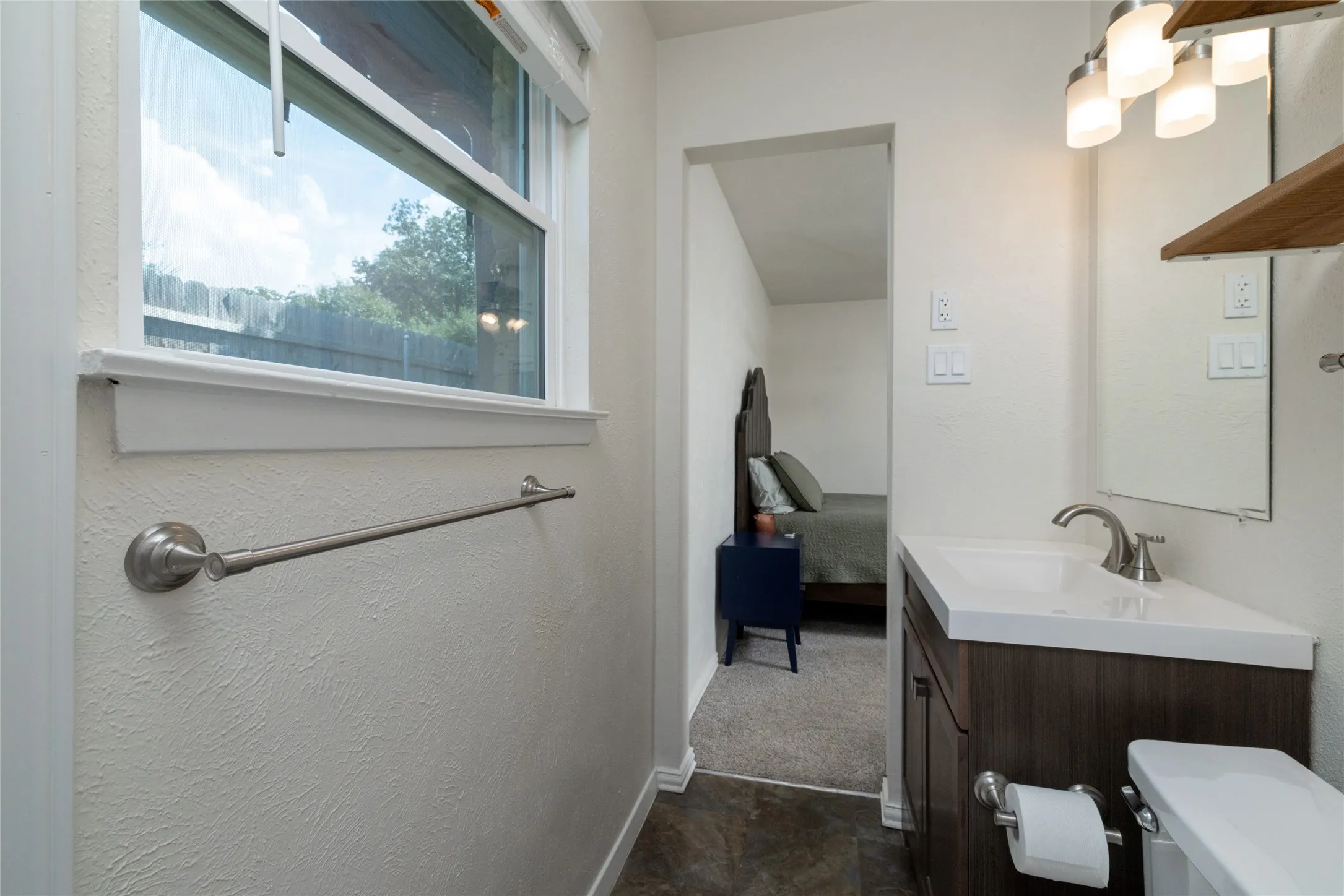 White single-hung window with trim, modern vanity with integrated sink, brushed nickel faucet, three-light vanity fixture, and wall-mounted mirror
