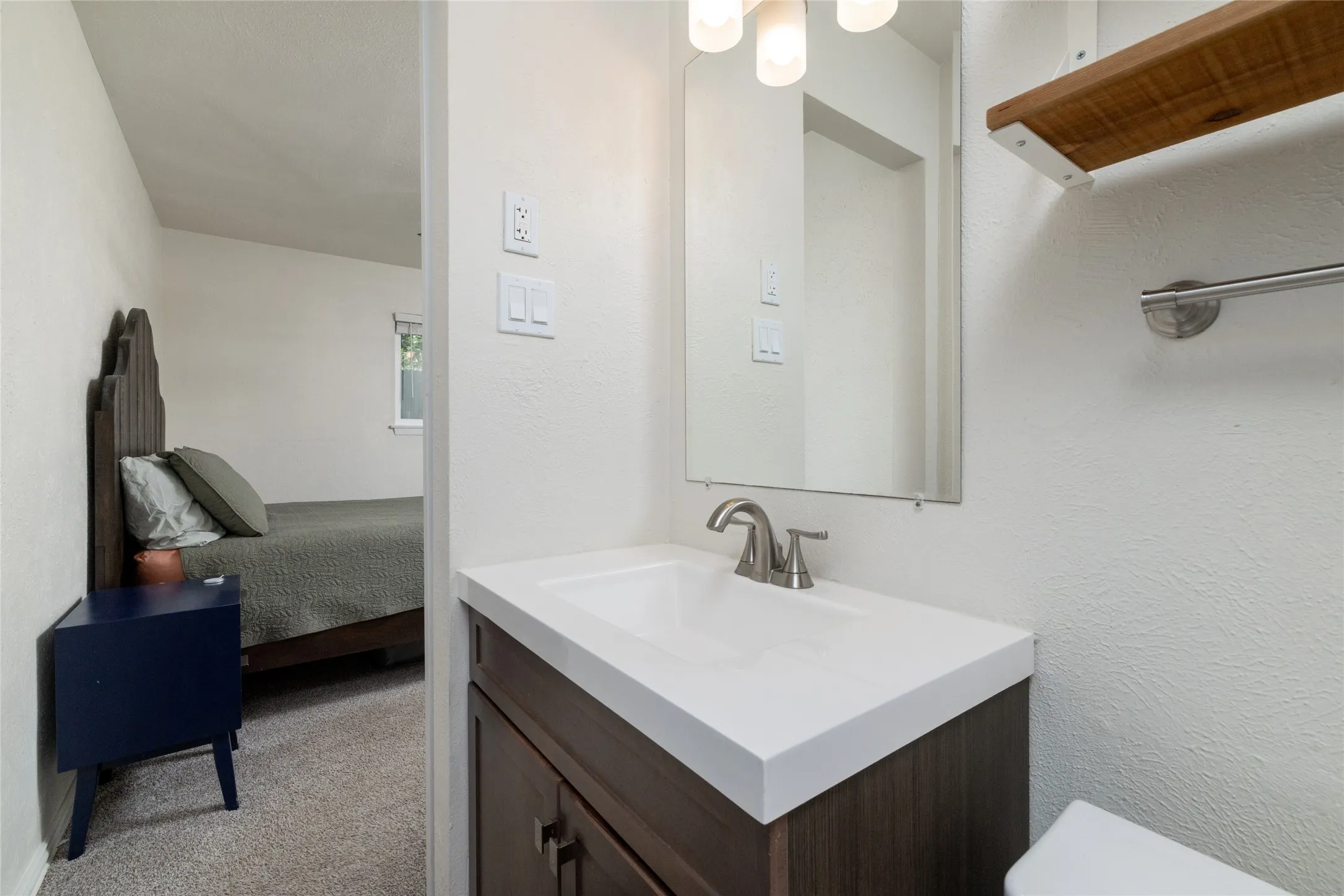 Vanity with integrated sink and brushed nickel faucet, wood-finish cabinet, wall-mounted mirror, and overhead light fixture