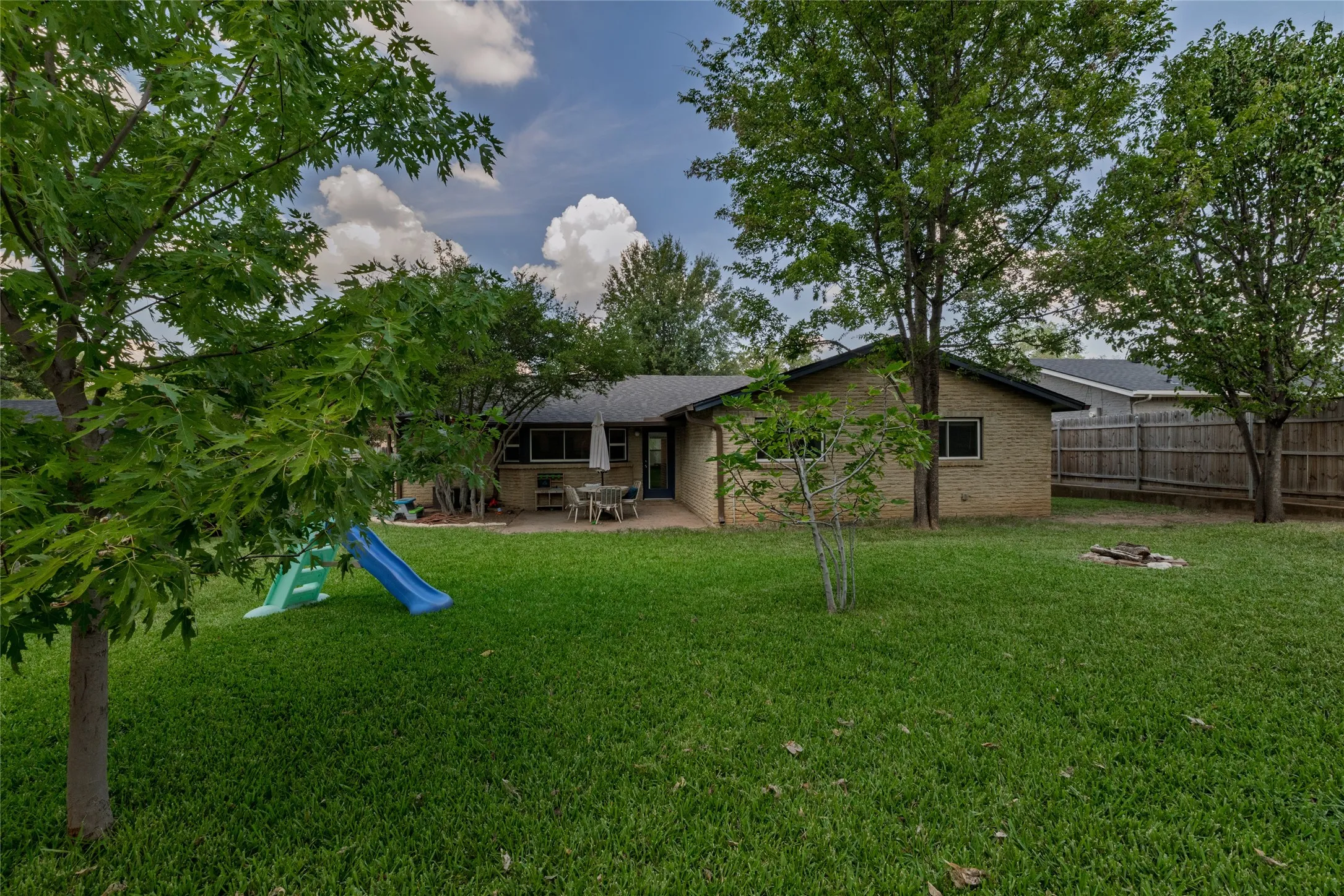 Expansive backyard featuring a manicured lawn, mature trees, and a brick exterior