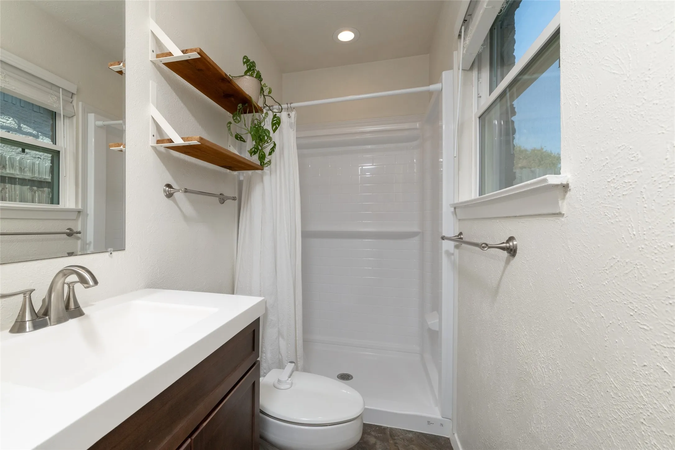 Integrated vanity with a single basin sink and brushed nickel faucet, walk-in shower, recessed lighting, and wall-mounted shelving