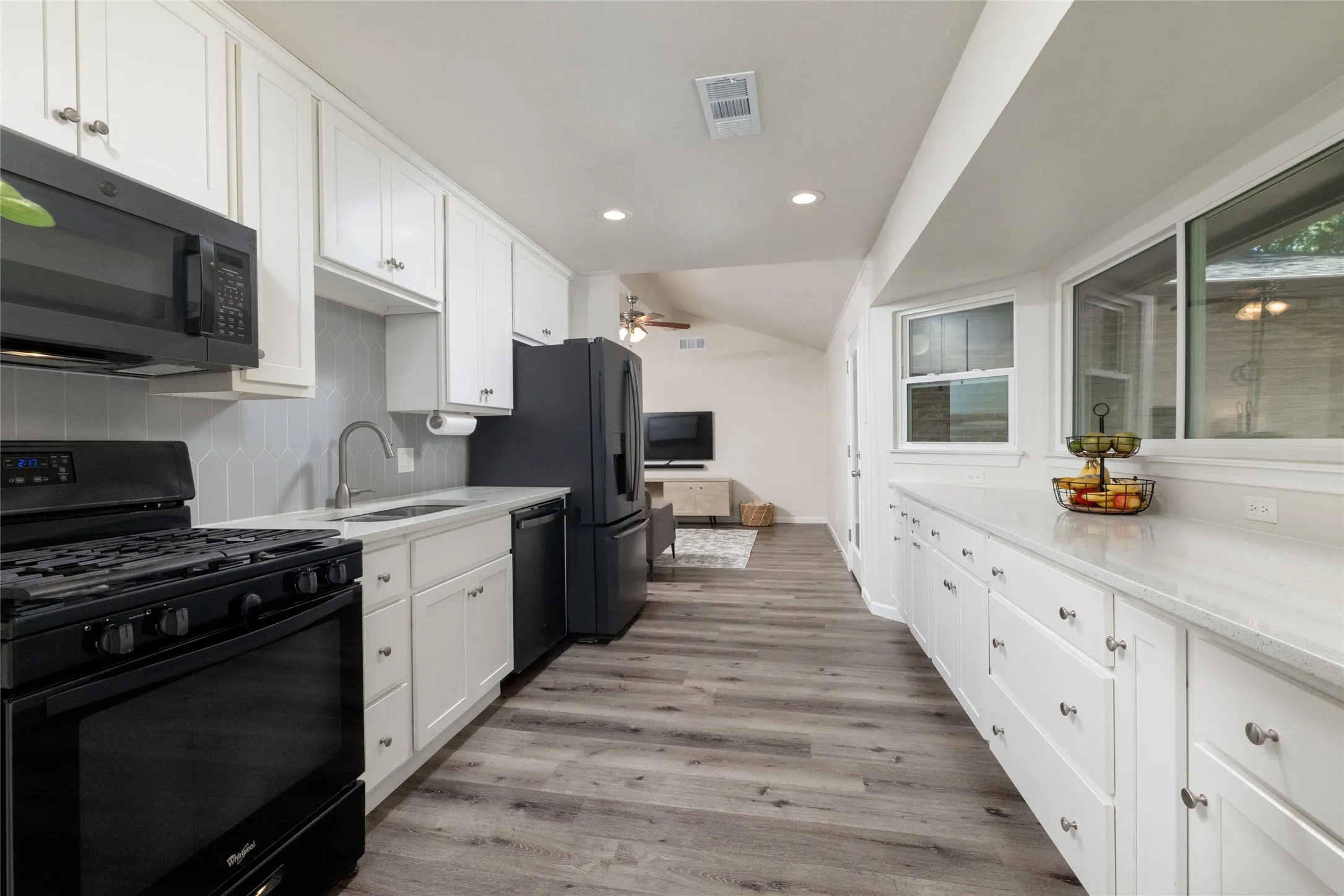 Galley kitchen with white cabinetry, light countertops, wood-finish flooring, recessed lighting, and black appliances
