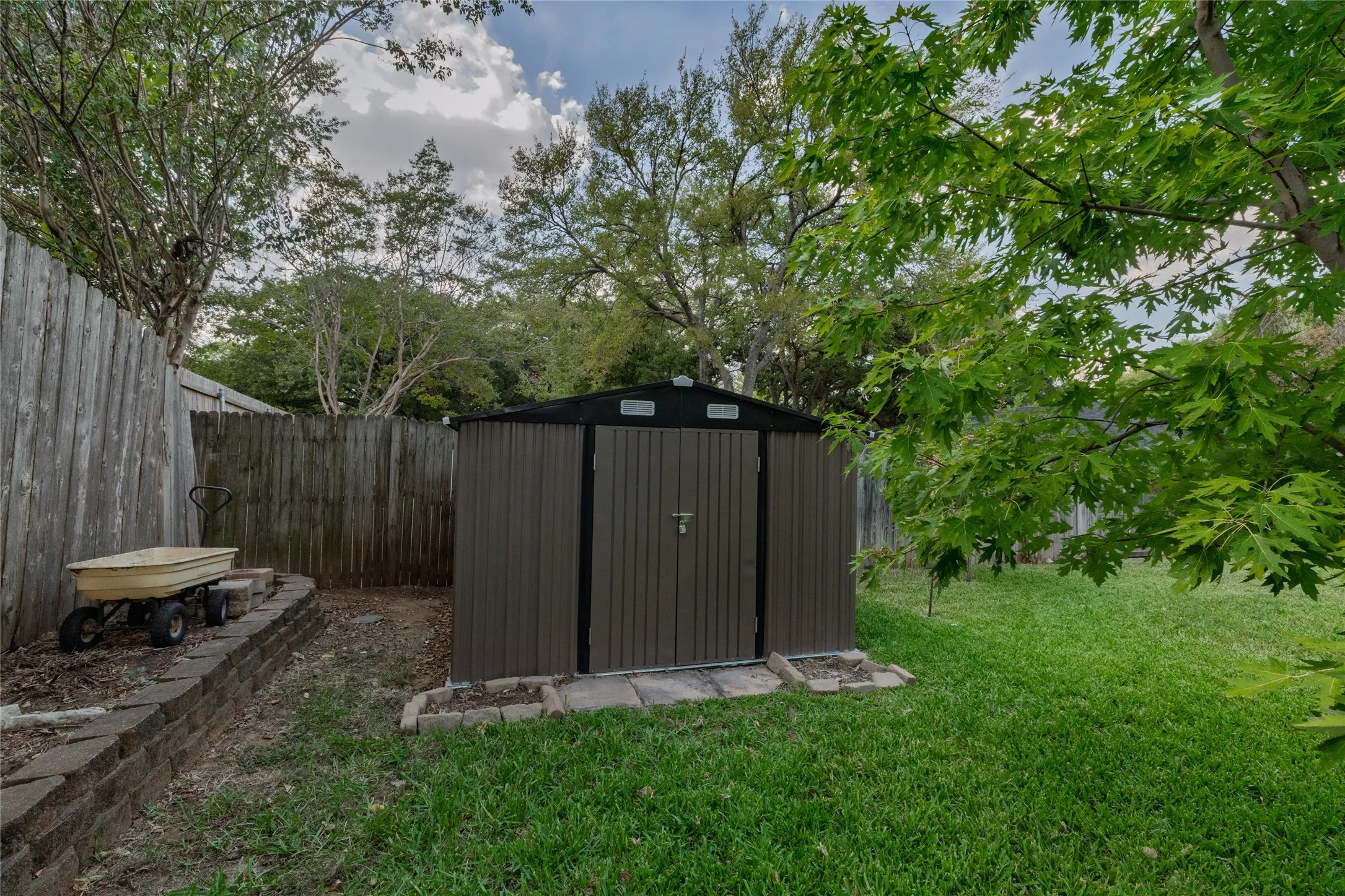 Detached storage shed with a peaked roof, established privacy fencing, and mature trees