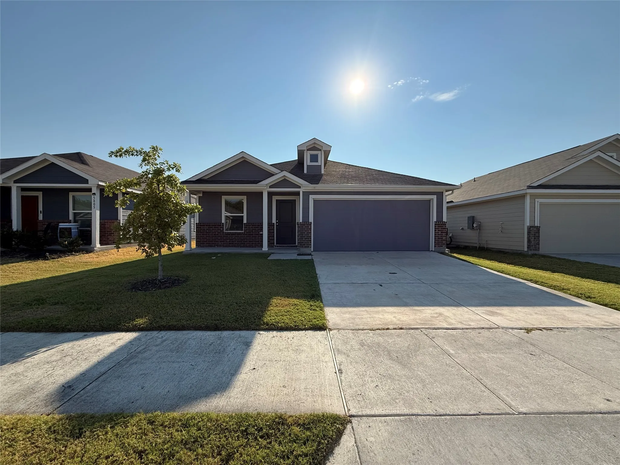 Single-story residence featuring a two-car garage, gray exterior siding, and brick accents