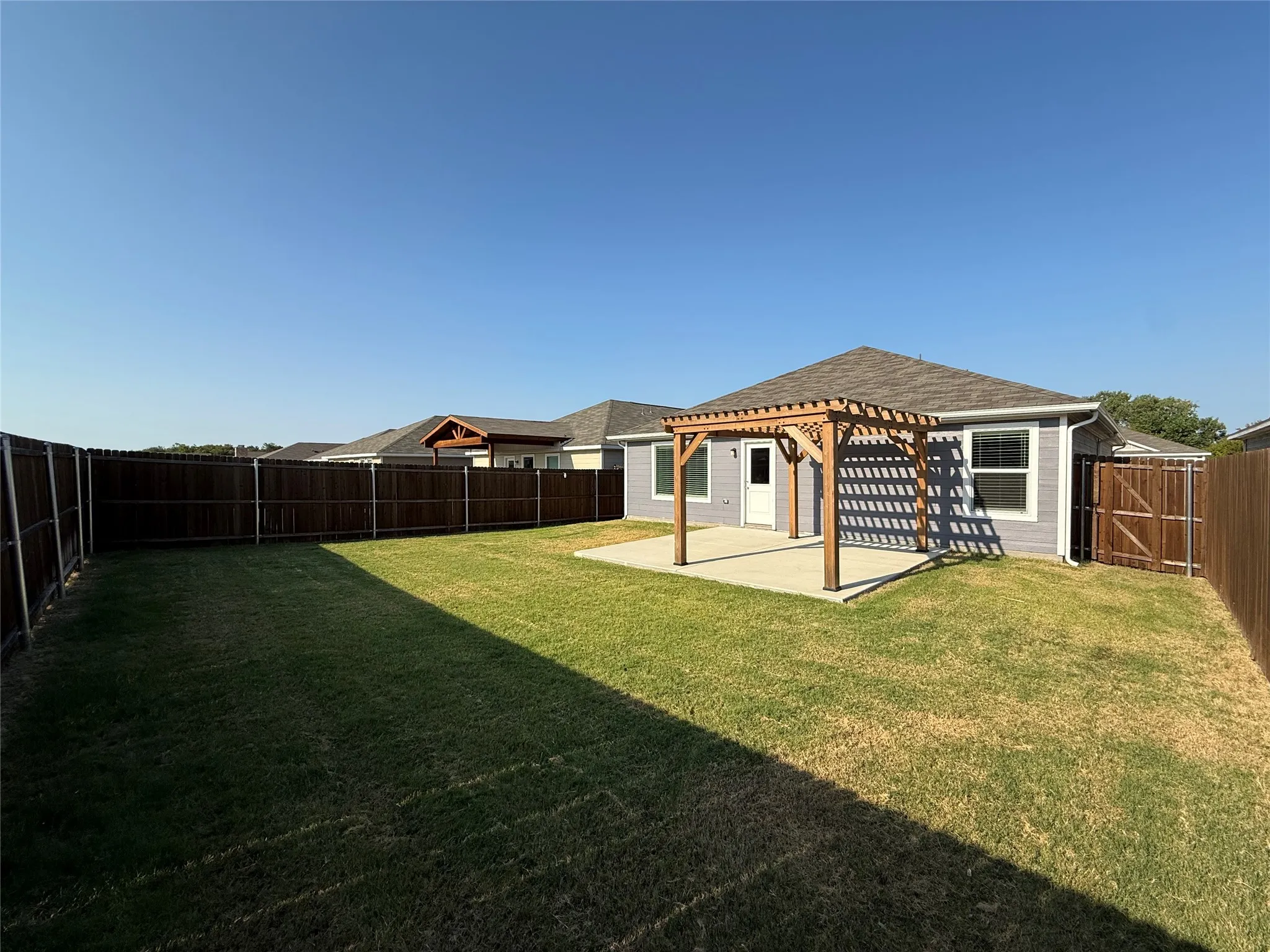 Spacious backyard featuring a wood pergola, concrete patio, privacy fence, and manicured lawn