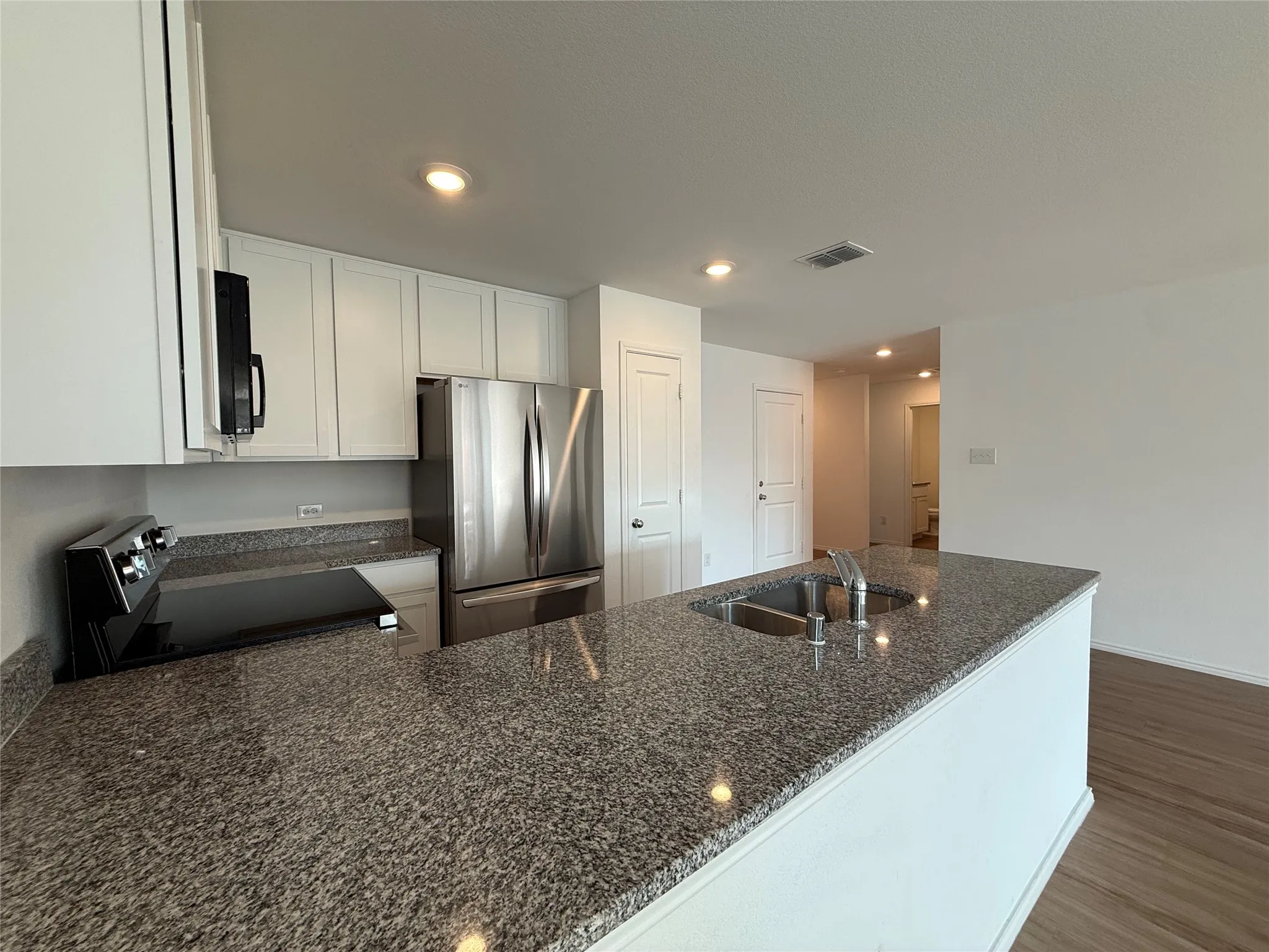 Kitchen featuring granite countertops, stainless steel appliances, white cabinetry, and a double basin sink