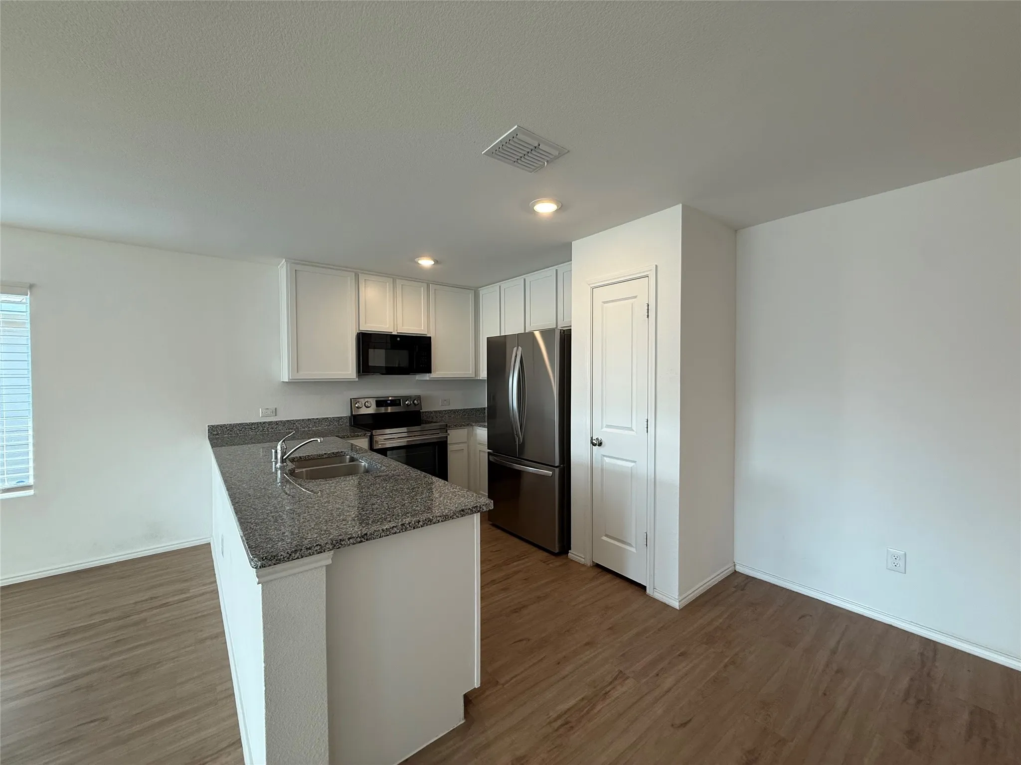 Kitchen with white cabinetry, stainless steel appliances, a center island with sink, granite countertops, and wood-finish flooring
