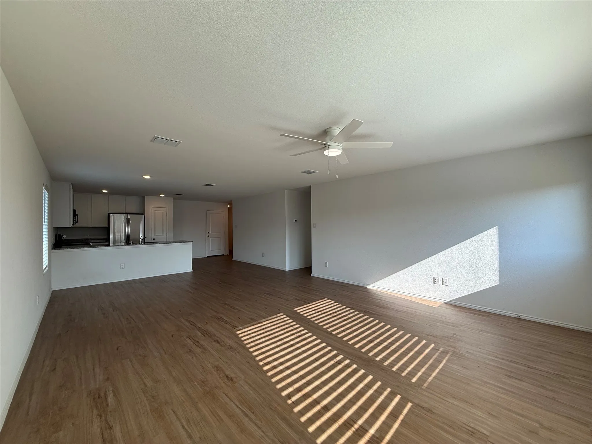 Open-concept living space with wood-finish flooring, white walls, and a ceiling fan