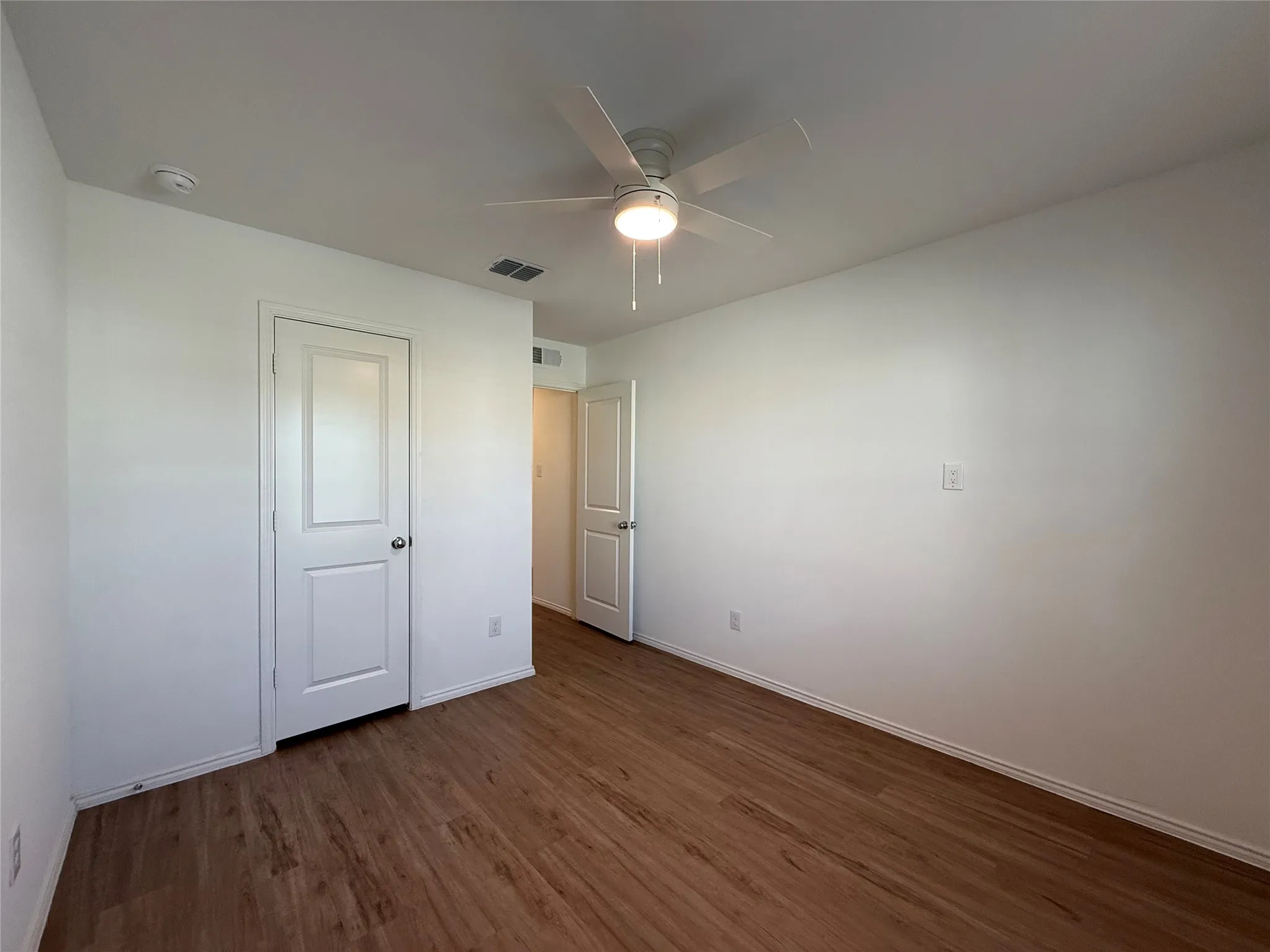 Wood-finish flooring, white paneled doors, ceiling fan with integrated lighting, and white walls