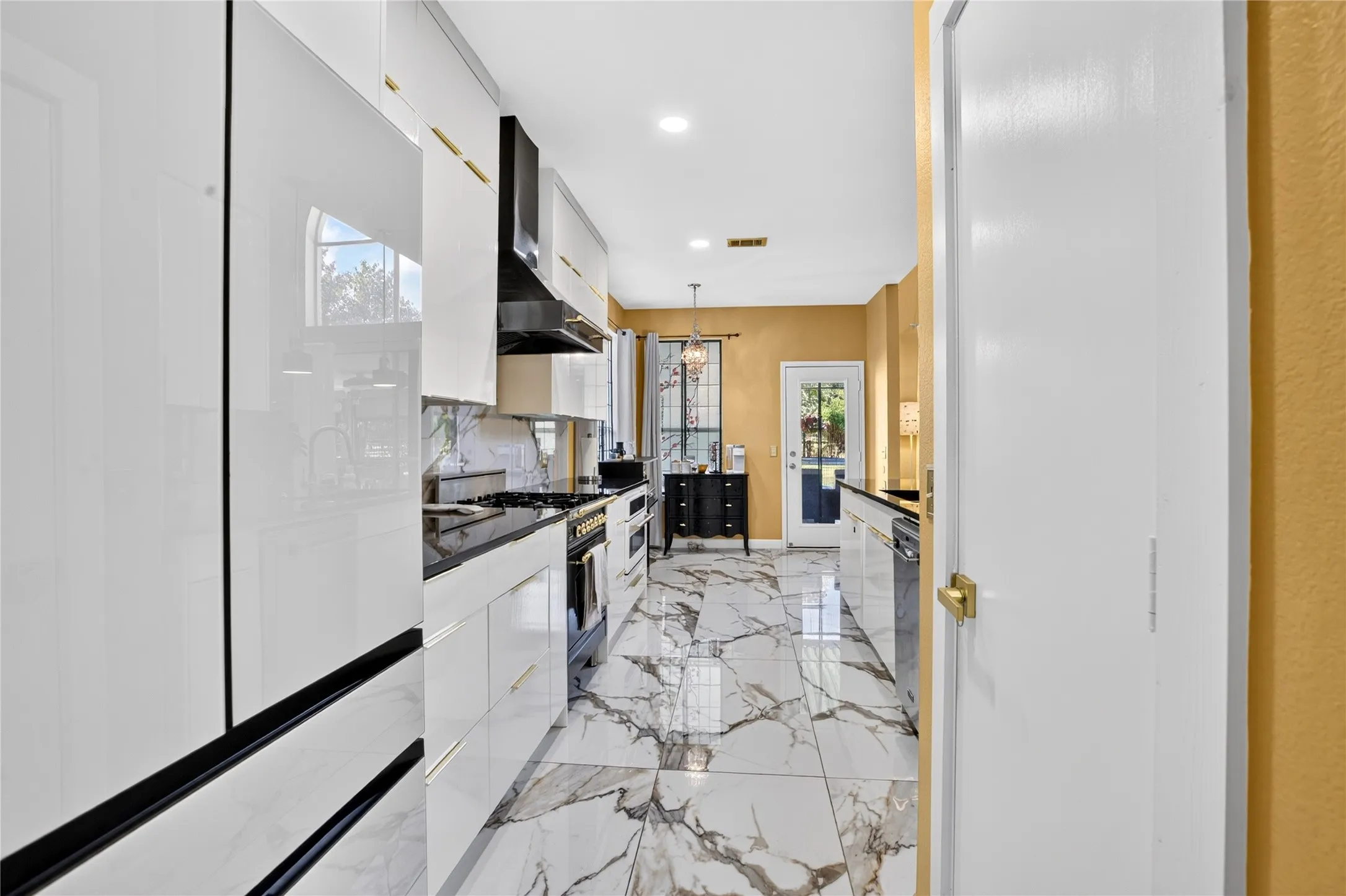 Gleaming tile flooring, white cabinetry with gold-finish hardware, dark countertops, built-in range, and a glass-paneled exterior door