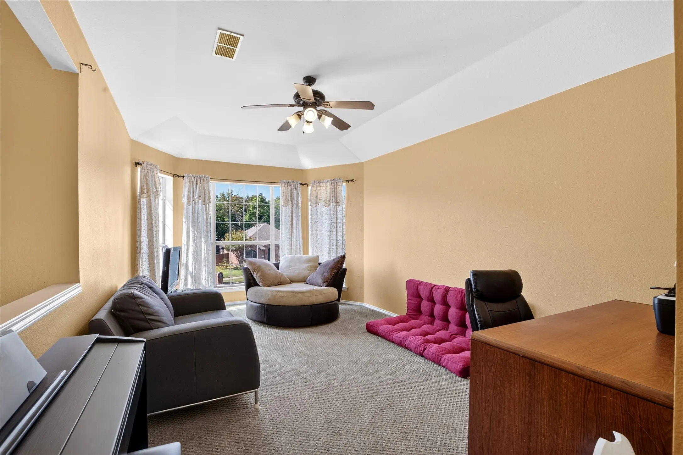 Tray ceiling with a ceiling fan light fixture, carpet flooring, and bay windows