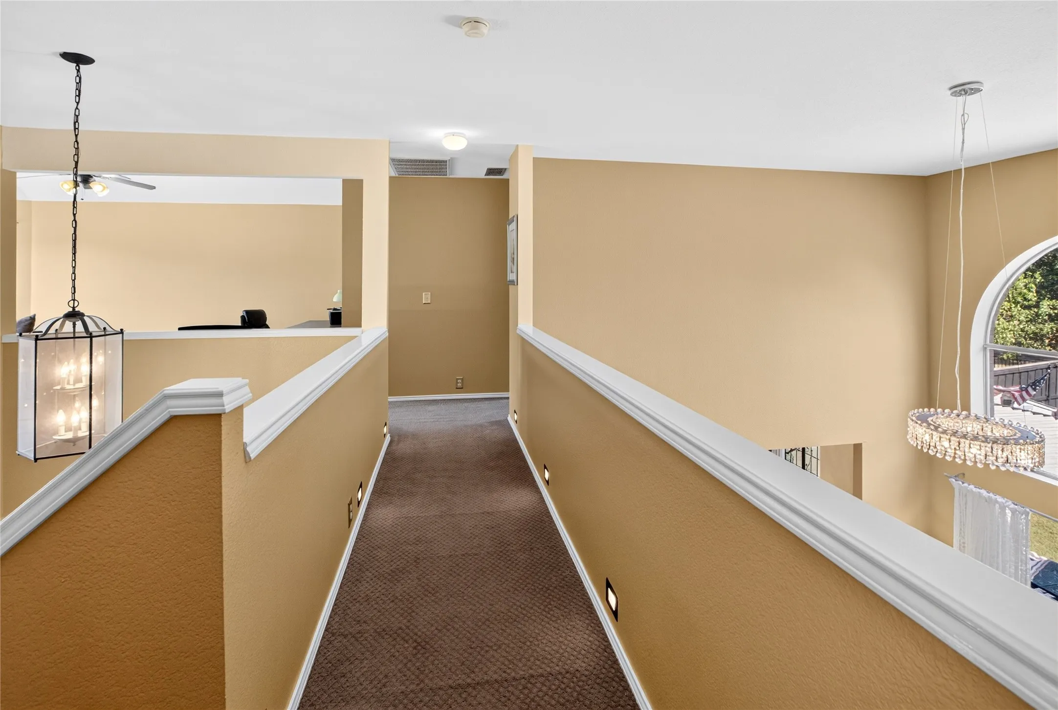 Carpeted hallway with integrated wall lighting, white railing, and a decorative pendant light