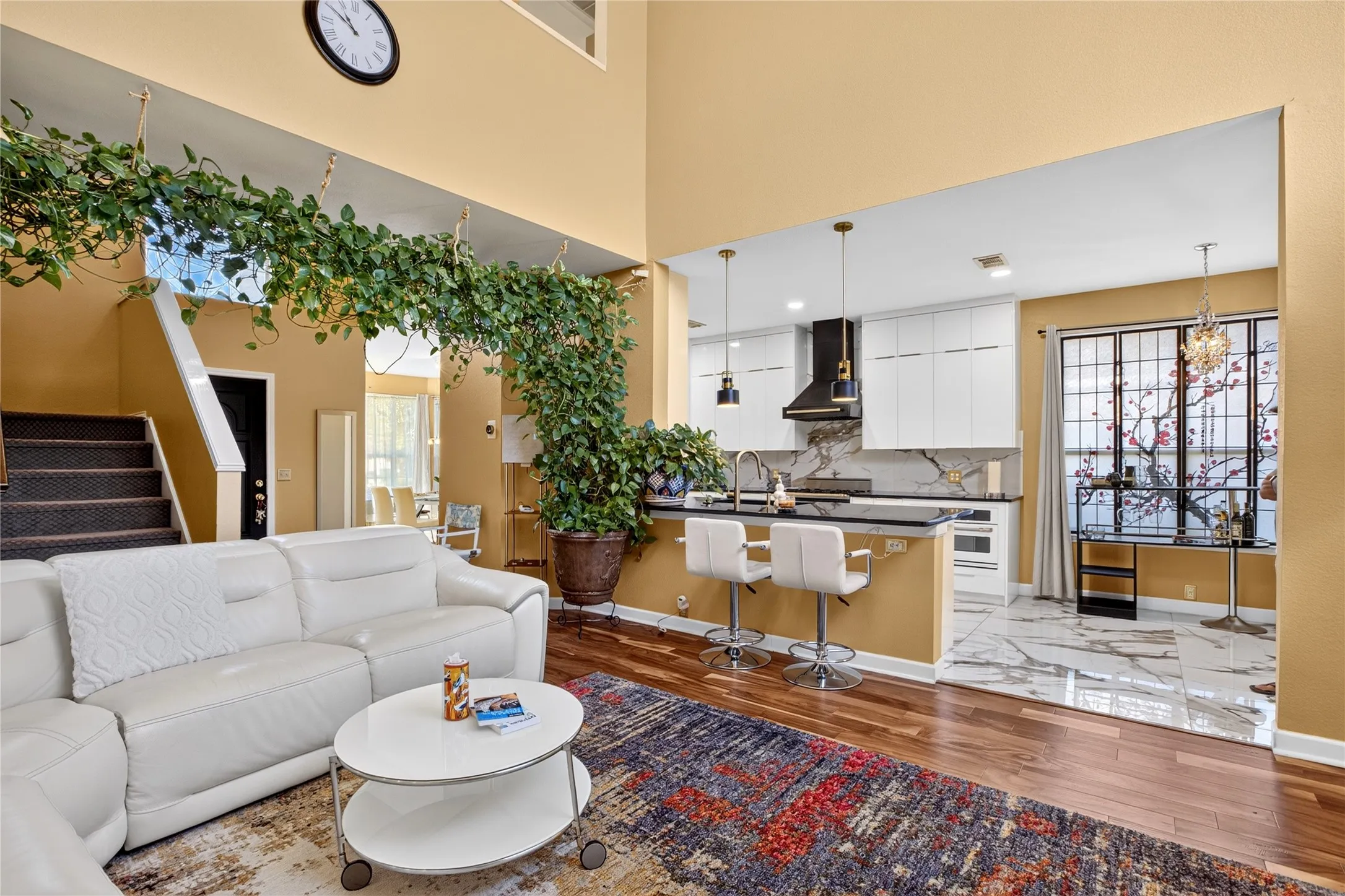 Open-concept living area with high ceilings, wood-finish flooring, and an integrated kitchen featuring a breakfast bar with pendant lighting, white cabinetry, and a dark range hood