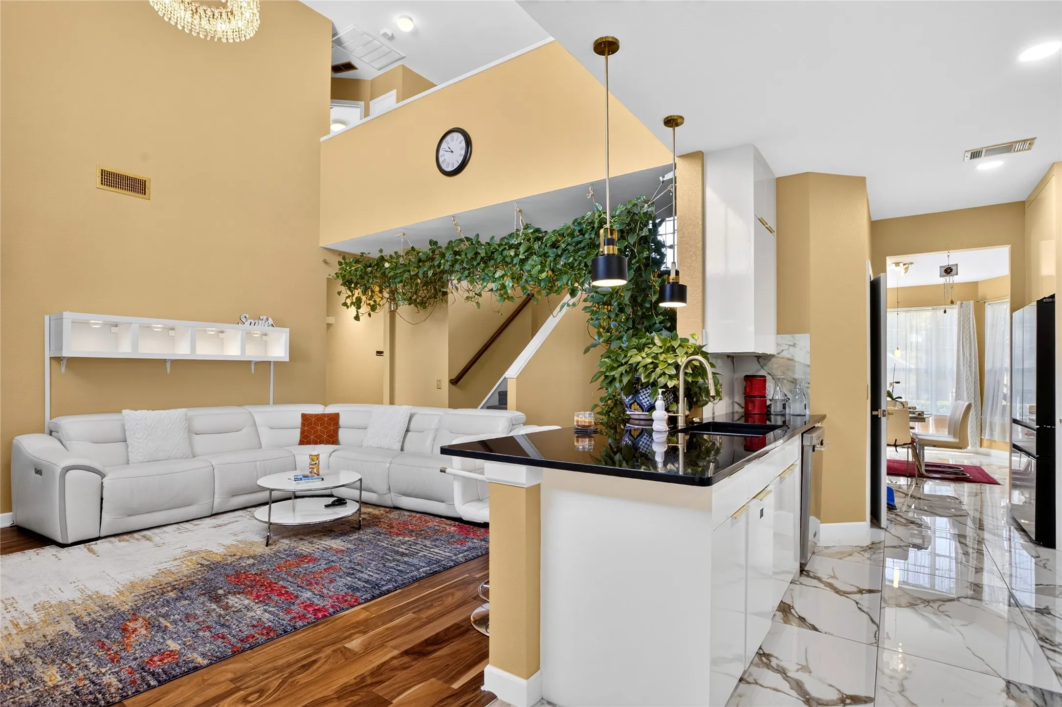 Two-story ceiling, wood-finish flooring, white kitchen cabinetry, black countertops, and polished tile flooring