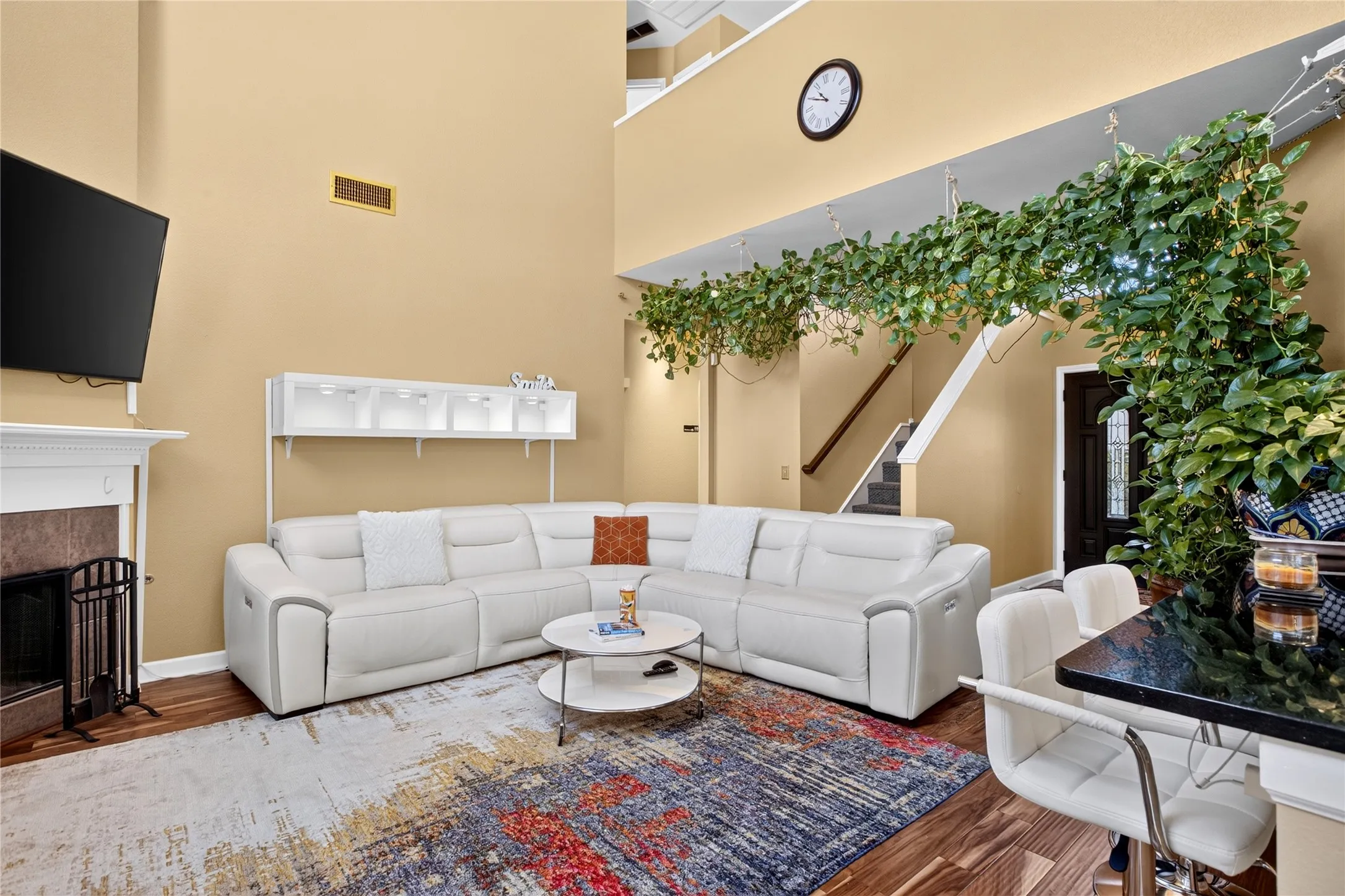 Double-height living space featuring wood-finish flooring, a fireplace with a stone surround, and an integrated built-in shelving unit