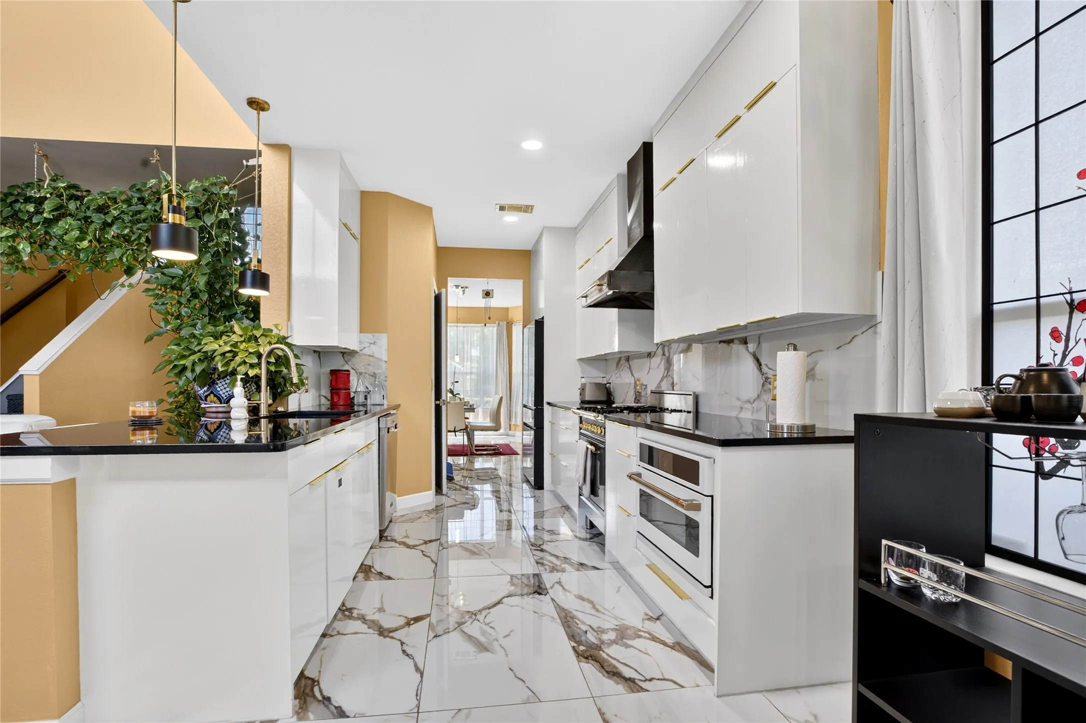 Galley kitchen featuring white cabinetry with gold-tone hardware, black countertops, and a white marble-patterned backsplash