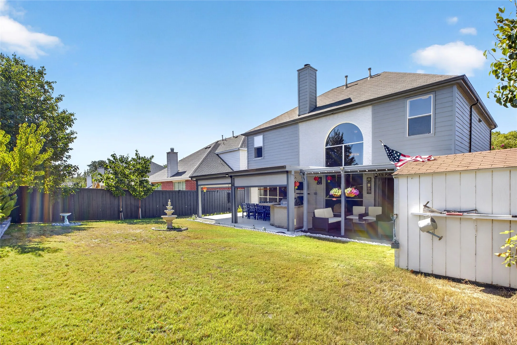 Expansive backyard featuring a covered patio, a detached storage shed, and a decorative fountain