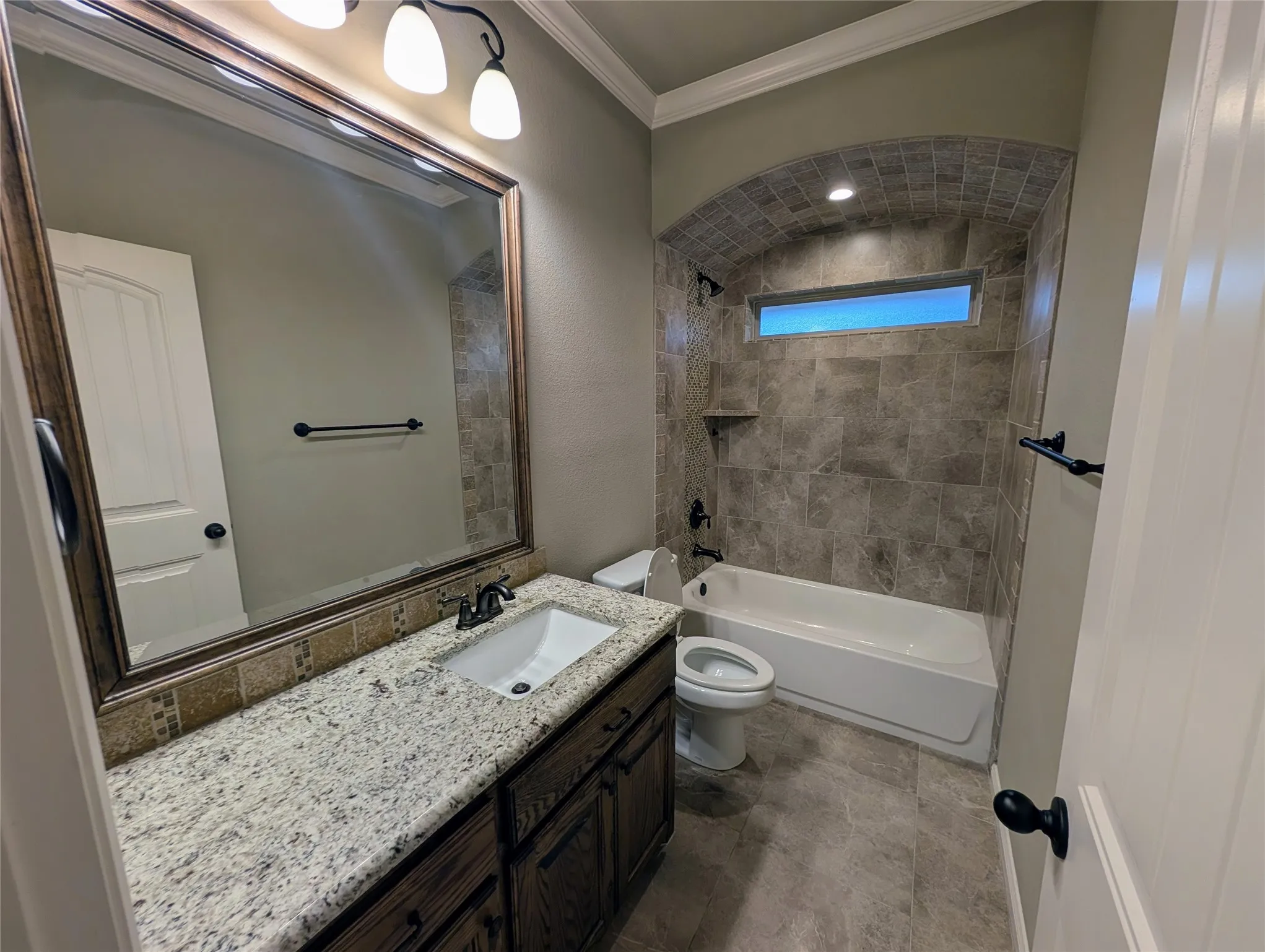 Vanity with a granite countertop and integrated sink, framed mirror, and a bathtub with tile surround and an arched alcove