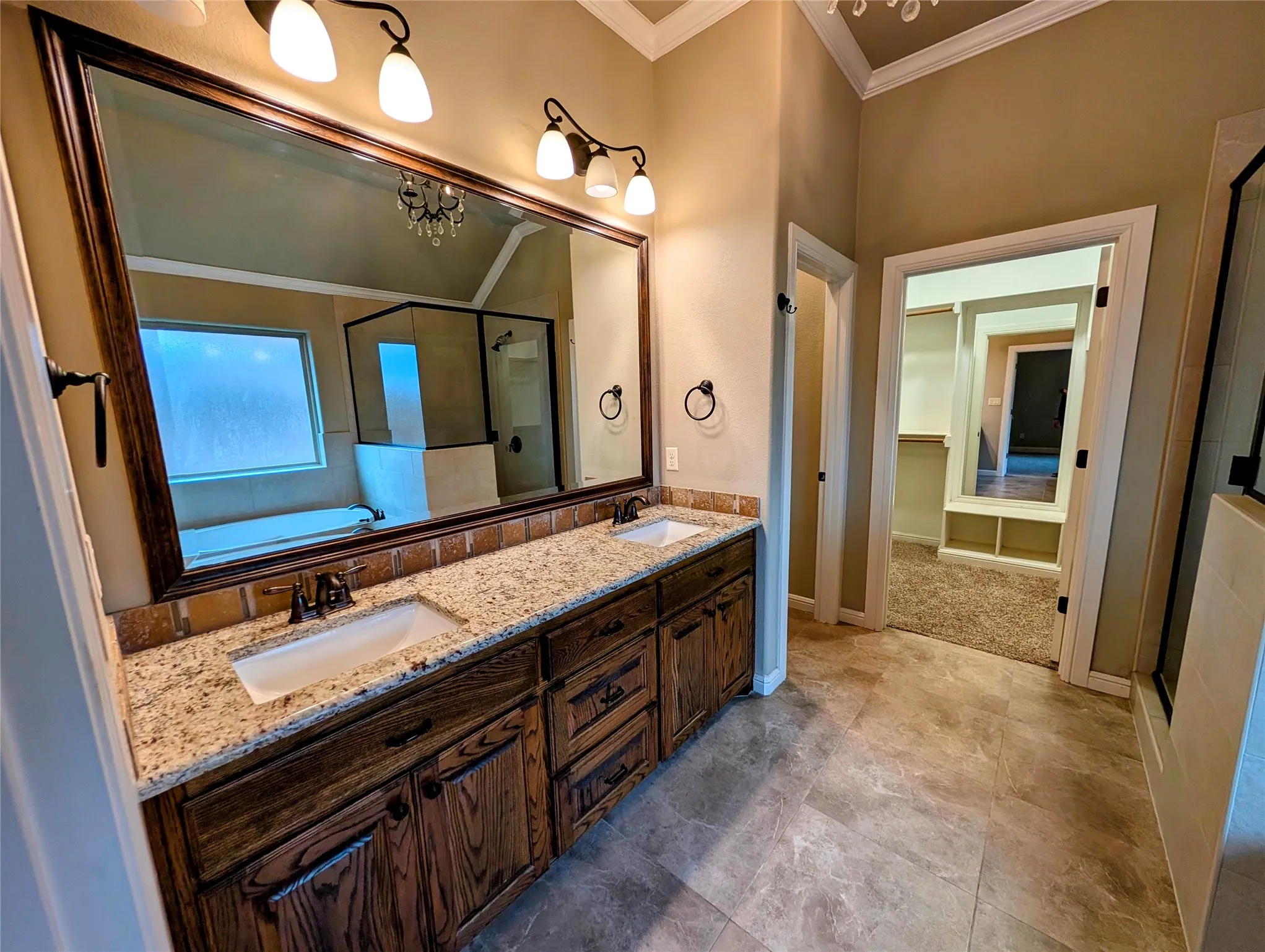 Dual vanity with granite countertops, wood-finish cabinetry, and a full-width mirror