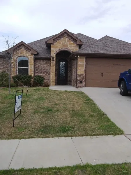 Brick and stone exterior featuring an arched entry, decorative front door, and an attached garage with a paved driveway