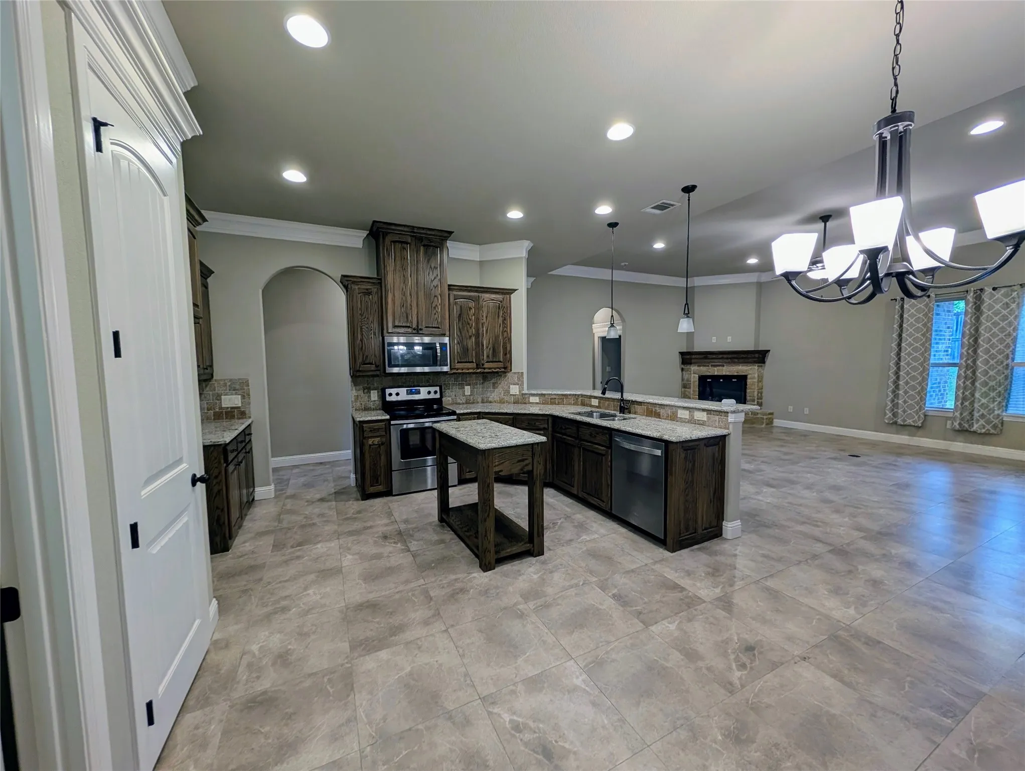 Spacious kitchen featuring dark wood cabinetry, stainless steel appliances, granite countertops, and an island with built-in storage