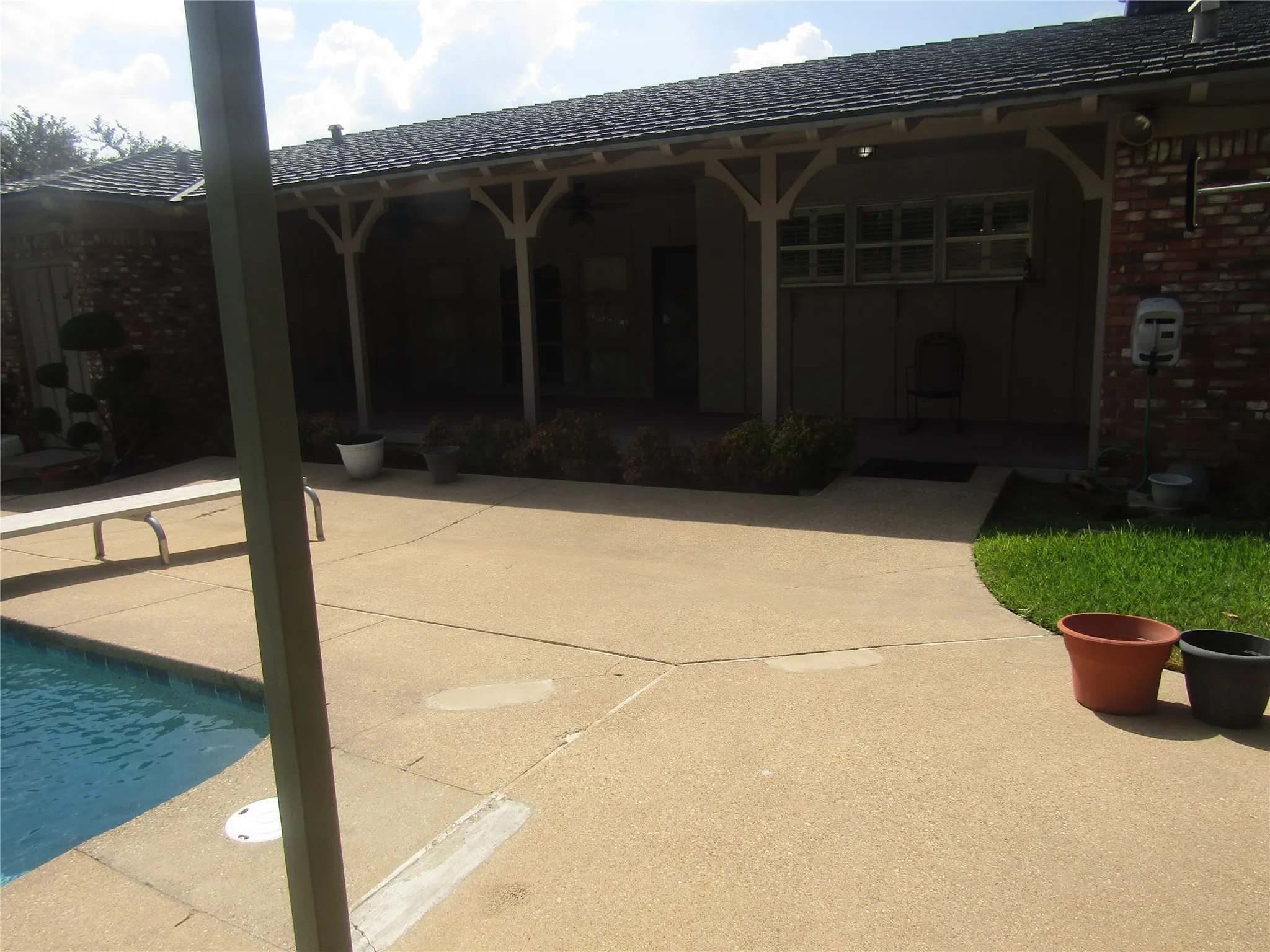 Brick exterior with an expansive patio featuring a covered walkway and an in-ground swimming pool