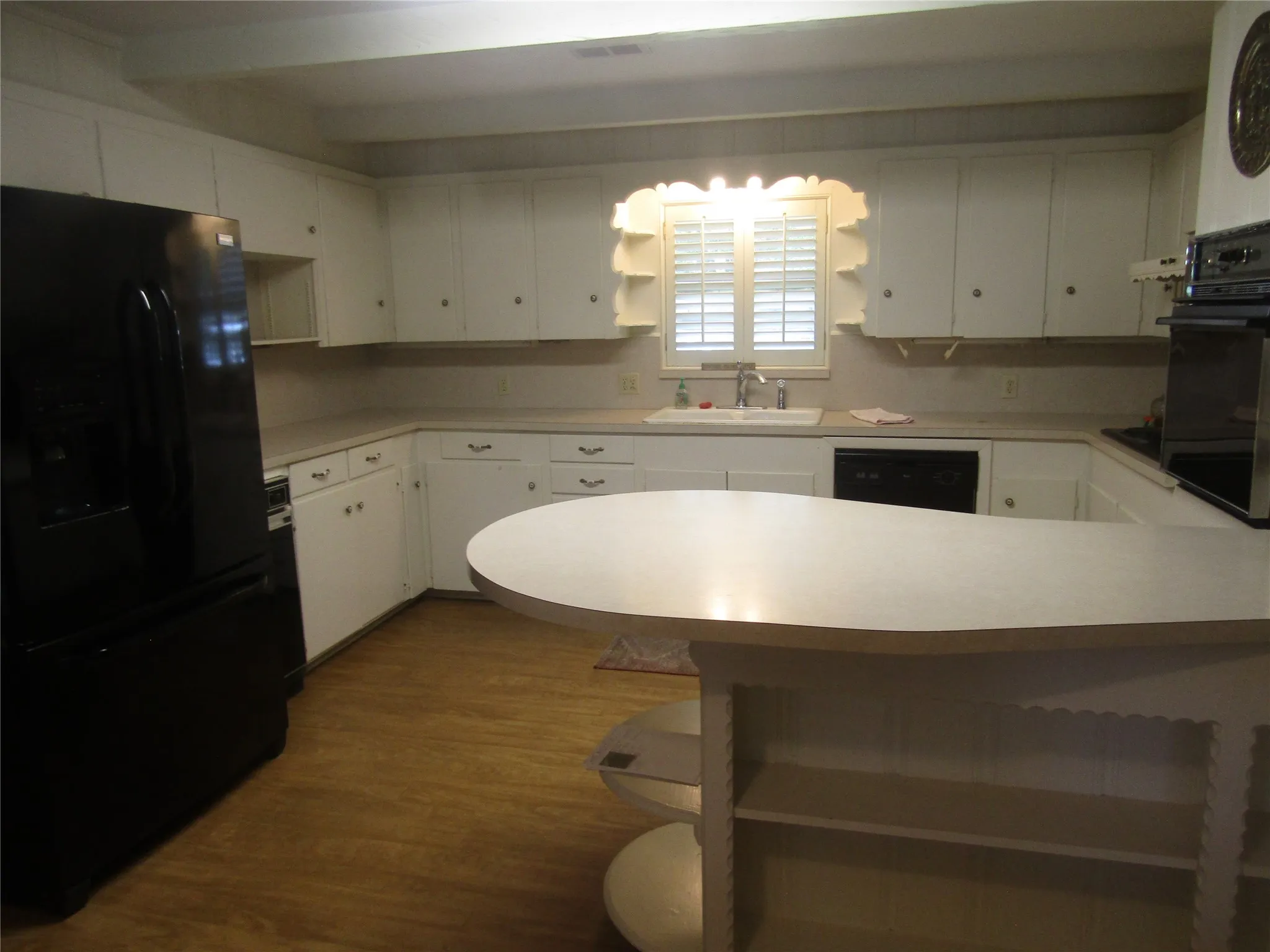 U-shaped kitchen layout featuring white cabinetry, wood-finish flooring, a built-in oven, and a peninsula with integrated shelving