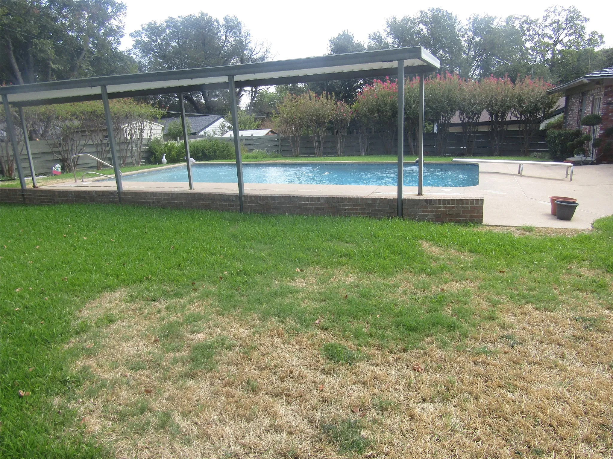 Pool with concrete surround, brick coping, and an overhead shade structure