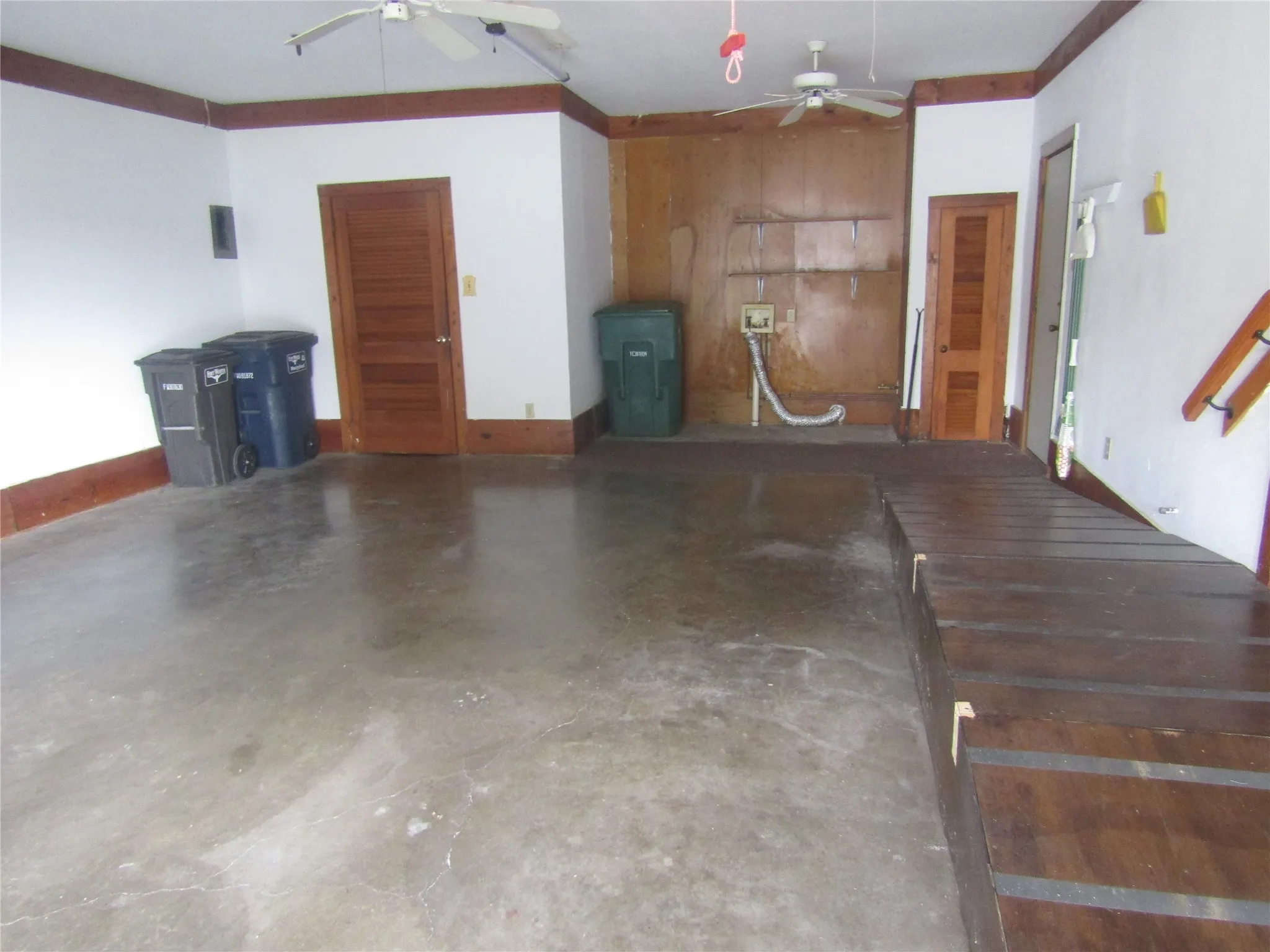 Spacious room featuring concrete flooring, wood paneling, and multiple wooden doors