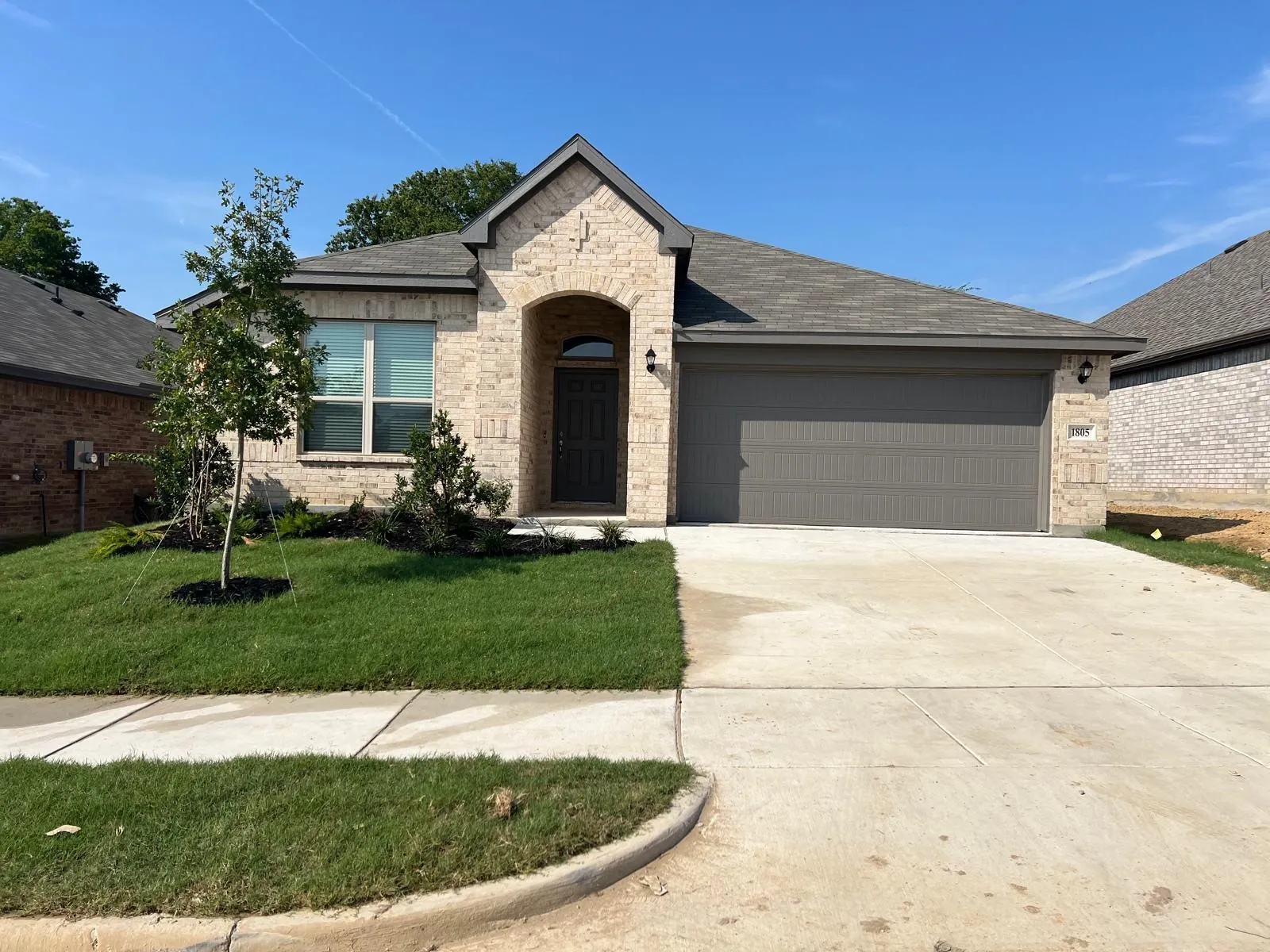 View of front of house featuring driveway, roof with shingles, a garage, brick siding, and a front lawn