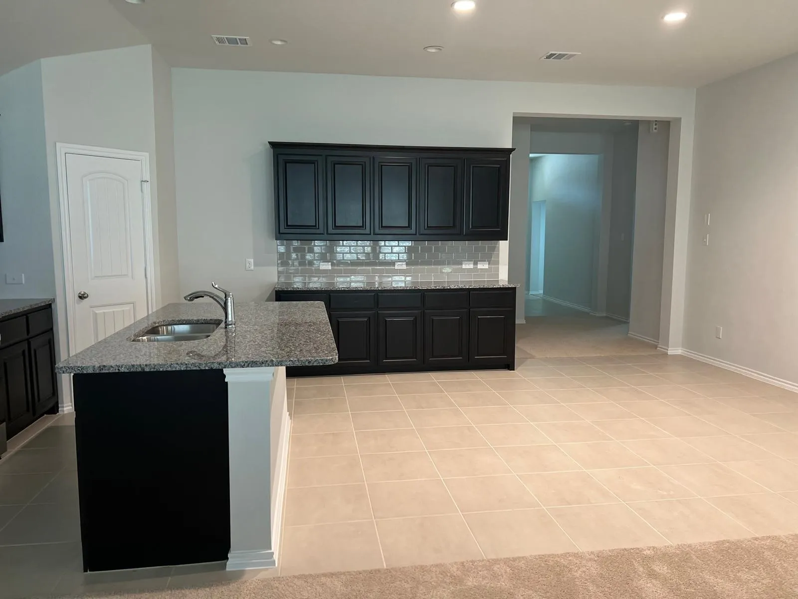 Kitchen featuring decorative backsplash, light tile patterned flooring, recessed lighting, dark stone counters, and a kitchen island with sink