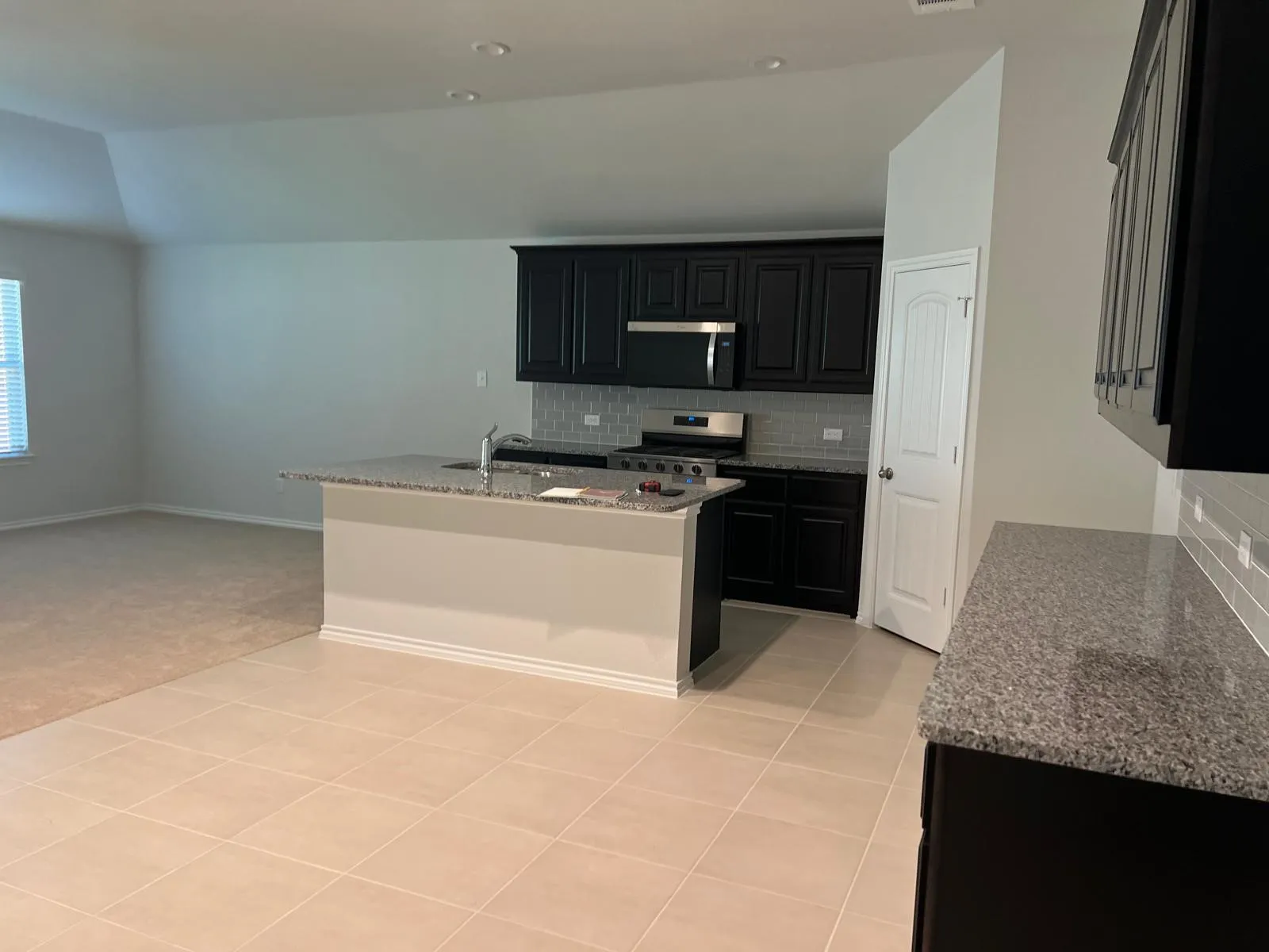 Kitchen with decorative backsplash, dark cabinetry, light stone counters, an island with sink, and appliances with stainless steel finishes