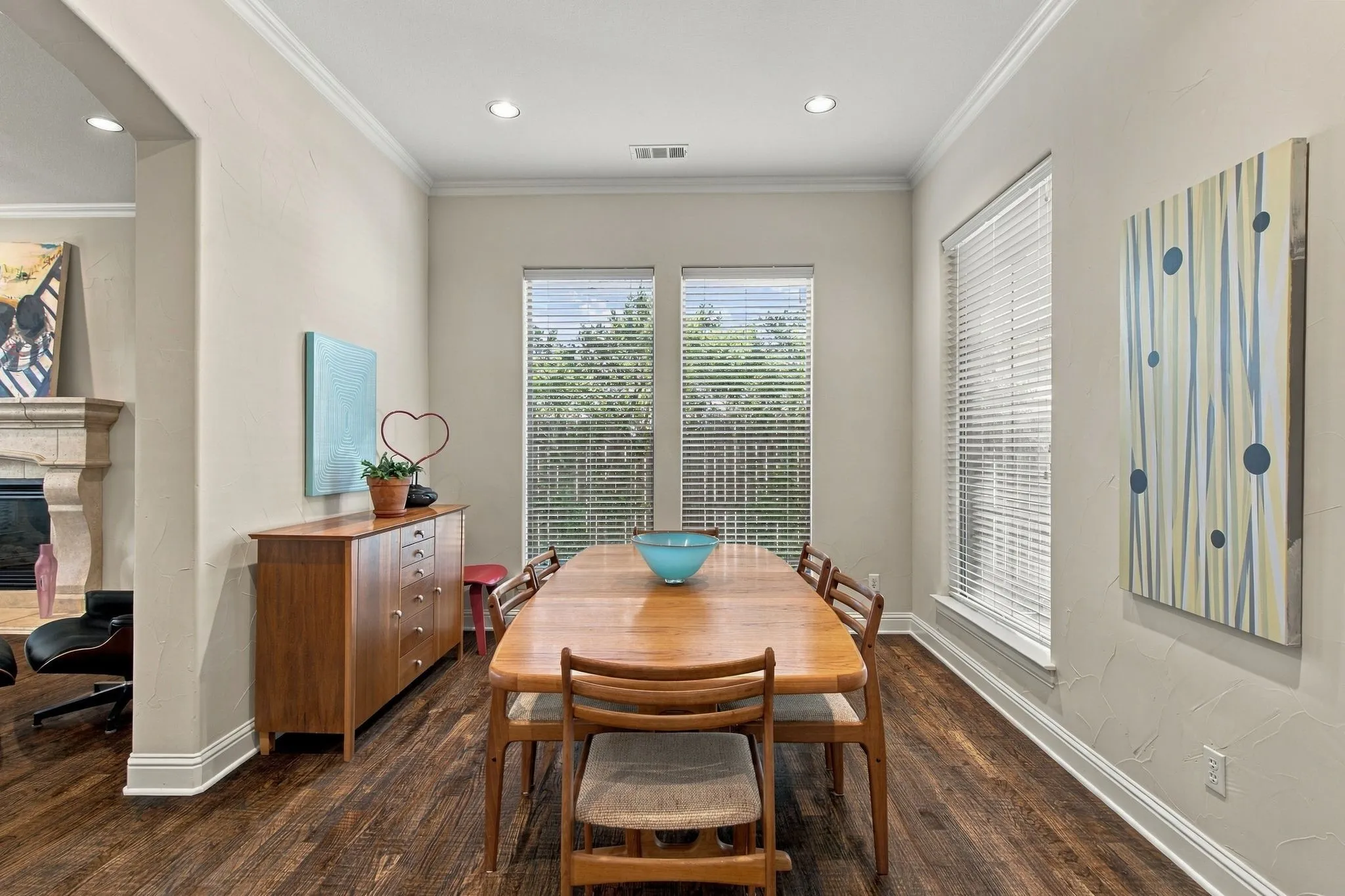 Wood-finish flooring throughout, crown molding, recessed lighting, multiple windows with blinds, and a stone fireplace surround
