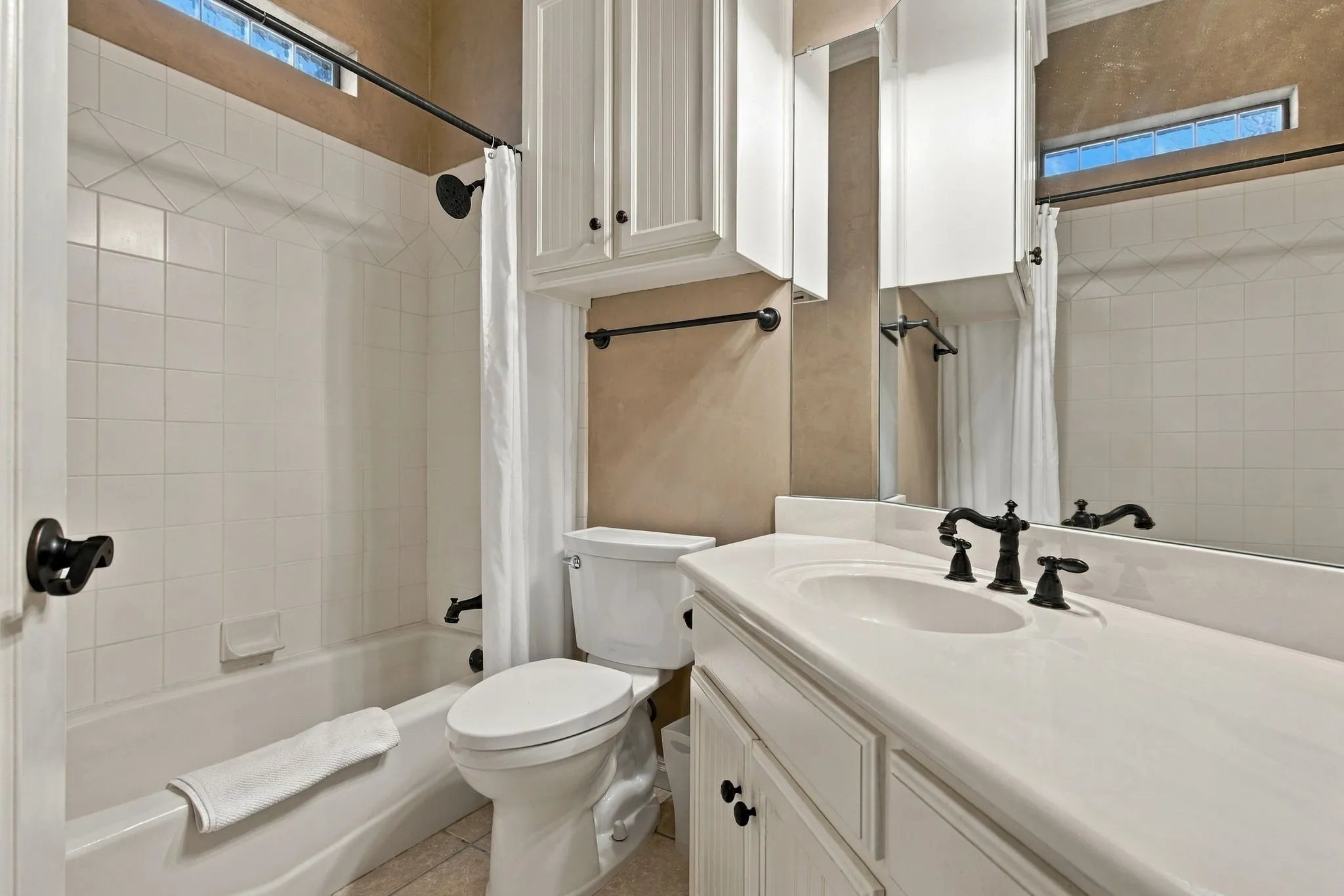 Bathroom featuring a white vanity with integrated sink, white cabinetry, dark bronze fixtures, and a tiled shower/tub combination
