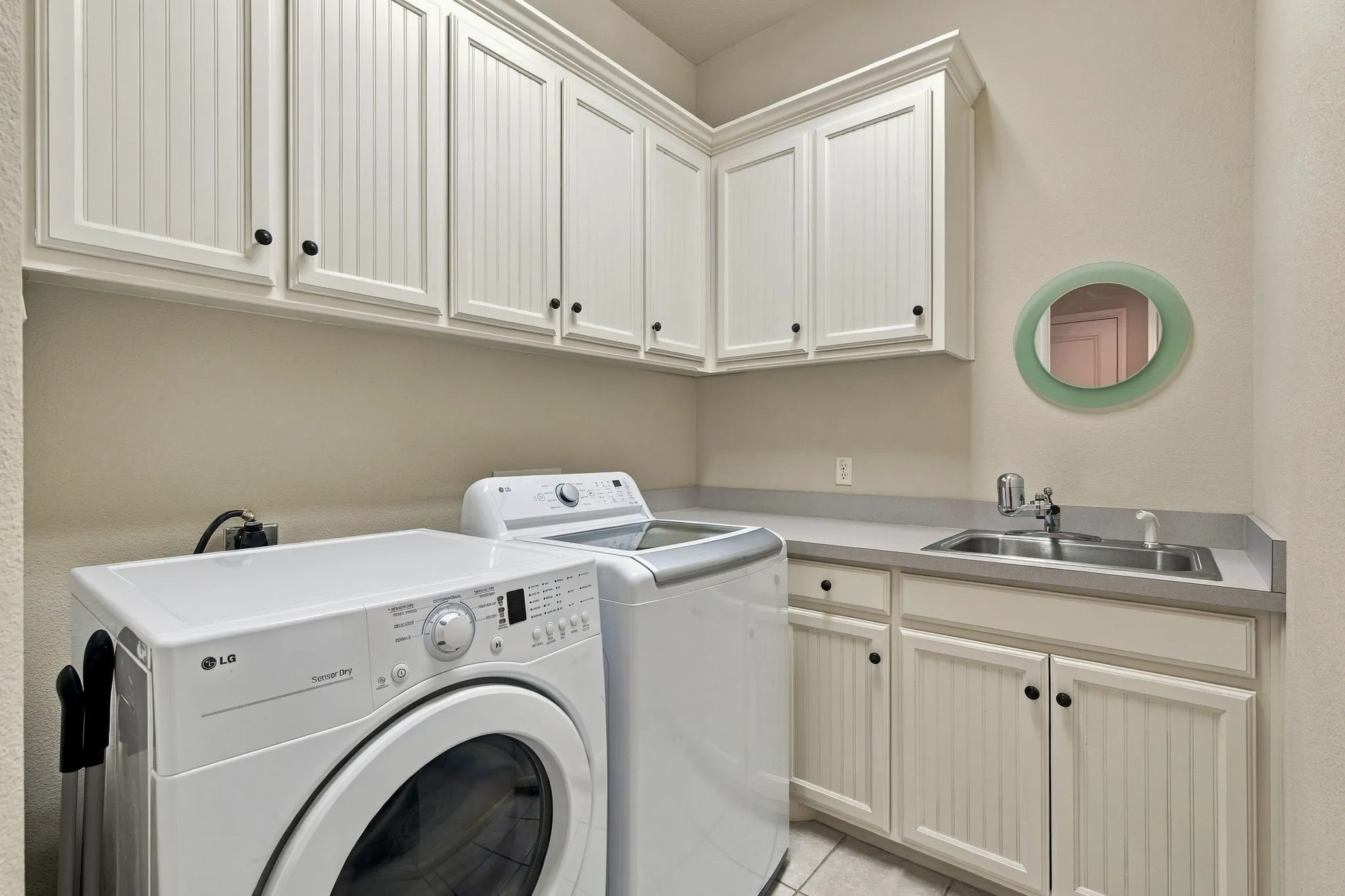 White shaker-style cabinetry with black hardware, integrated utility sink, light-toned countertop, and tile flooring