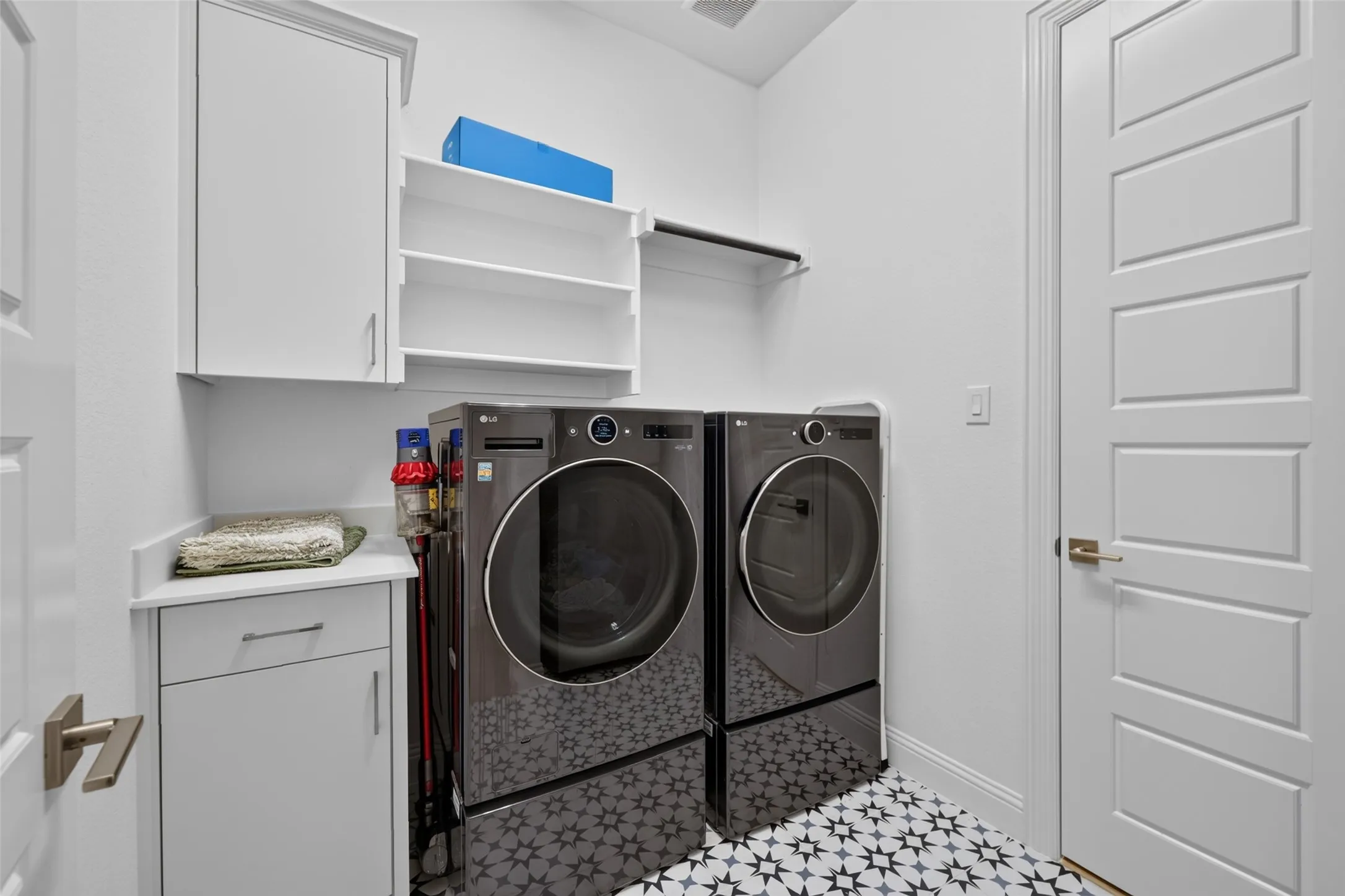 Integrated laundry area featuring white cabinetry, open shelving, a white countertop, and patterned floor tiling