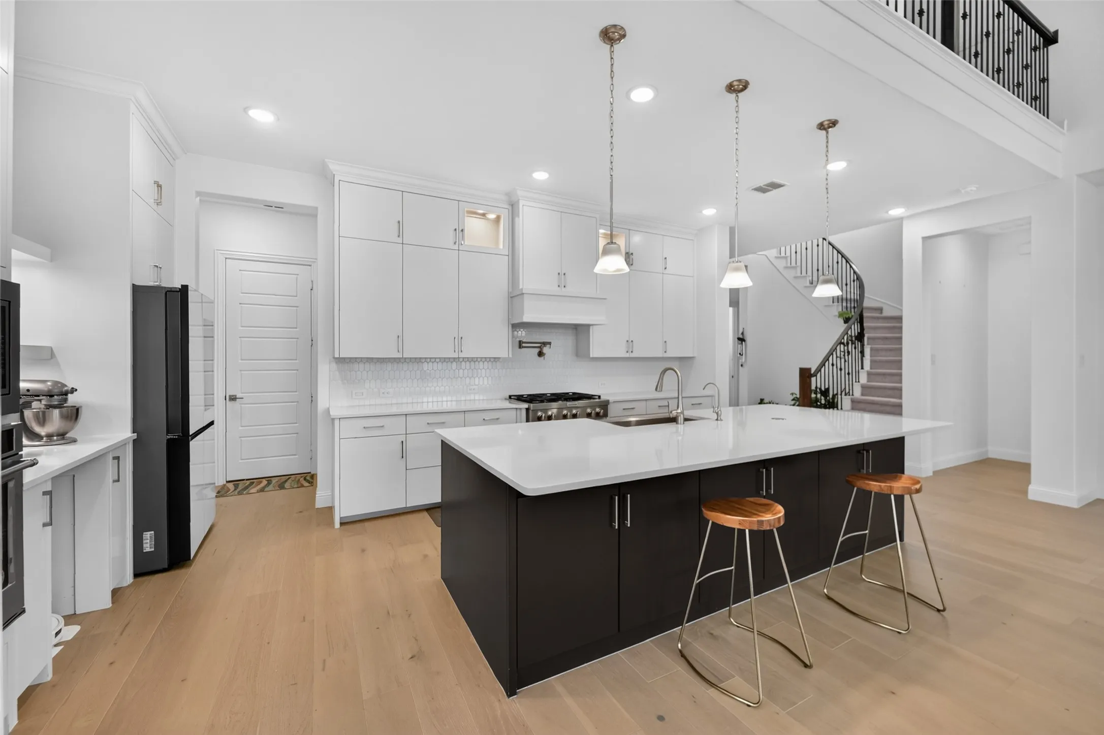Gourmet kitchen with a large central island, white shaker cabinetry, stainless steel appliances, and wood-finish flooring