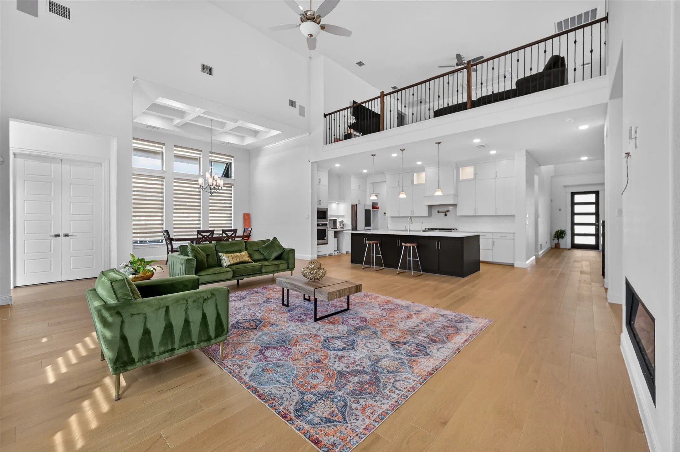 Open-concept living area featuring high ceilings, wood-finish flooring, a contemporary kitchen island with seating, a built-in fireplace, and an upper-level balcony overlooking the space