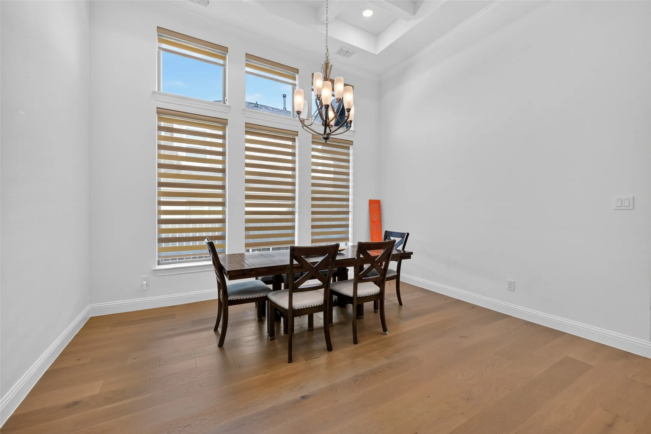 Hardwood flooring, high ceilings, layered window treatments, a coffered ceiling, and an ornate chandelier