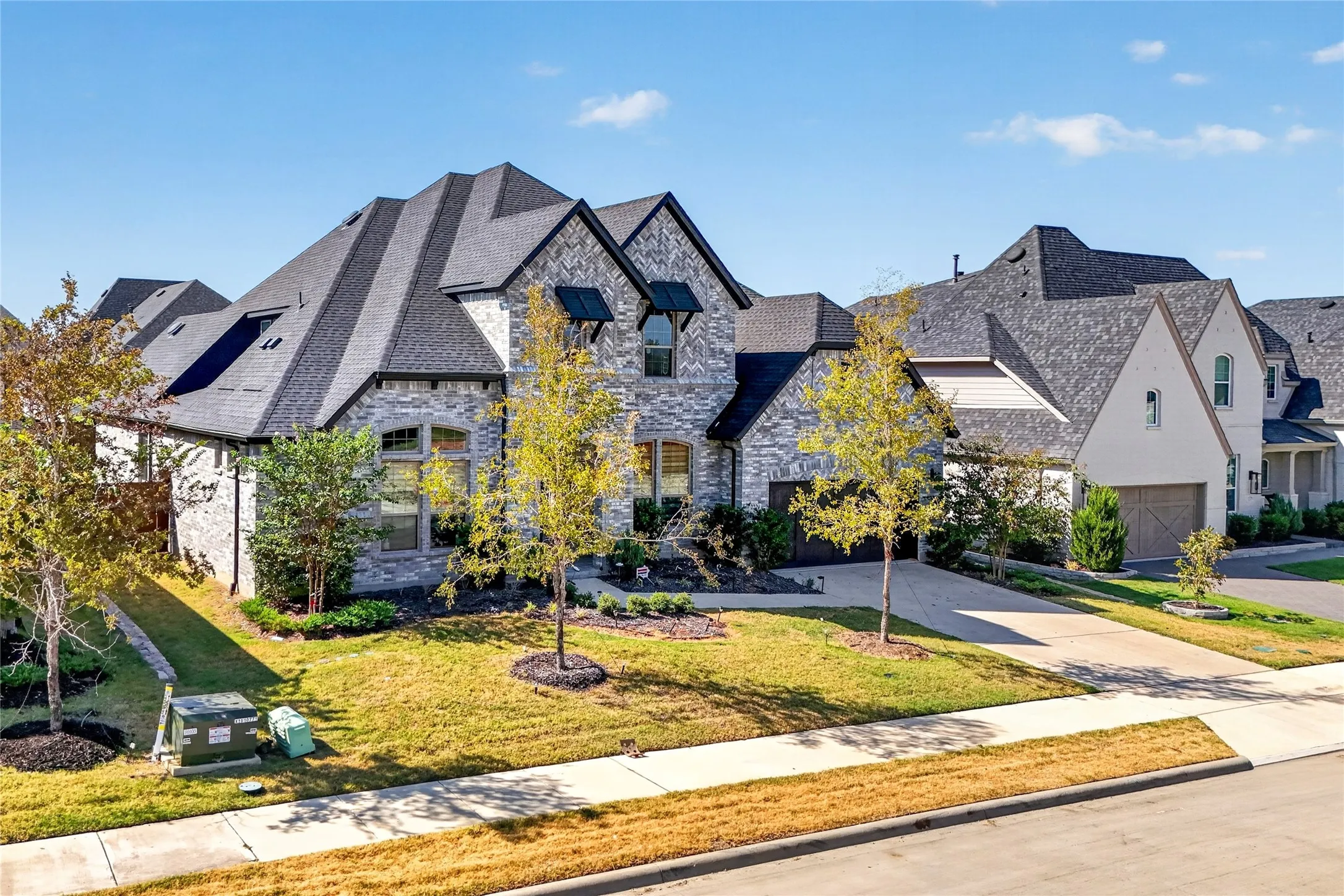 Stone exterior with dark shingle roof, arched garage door, and mature landscaping