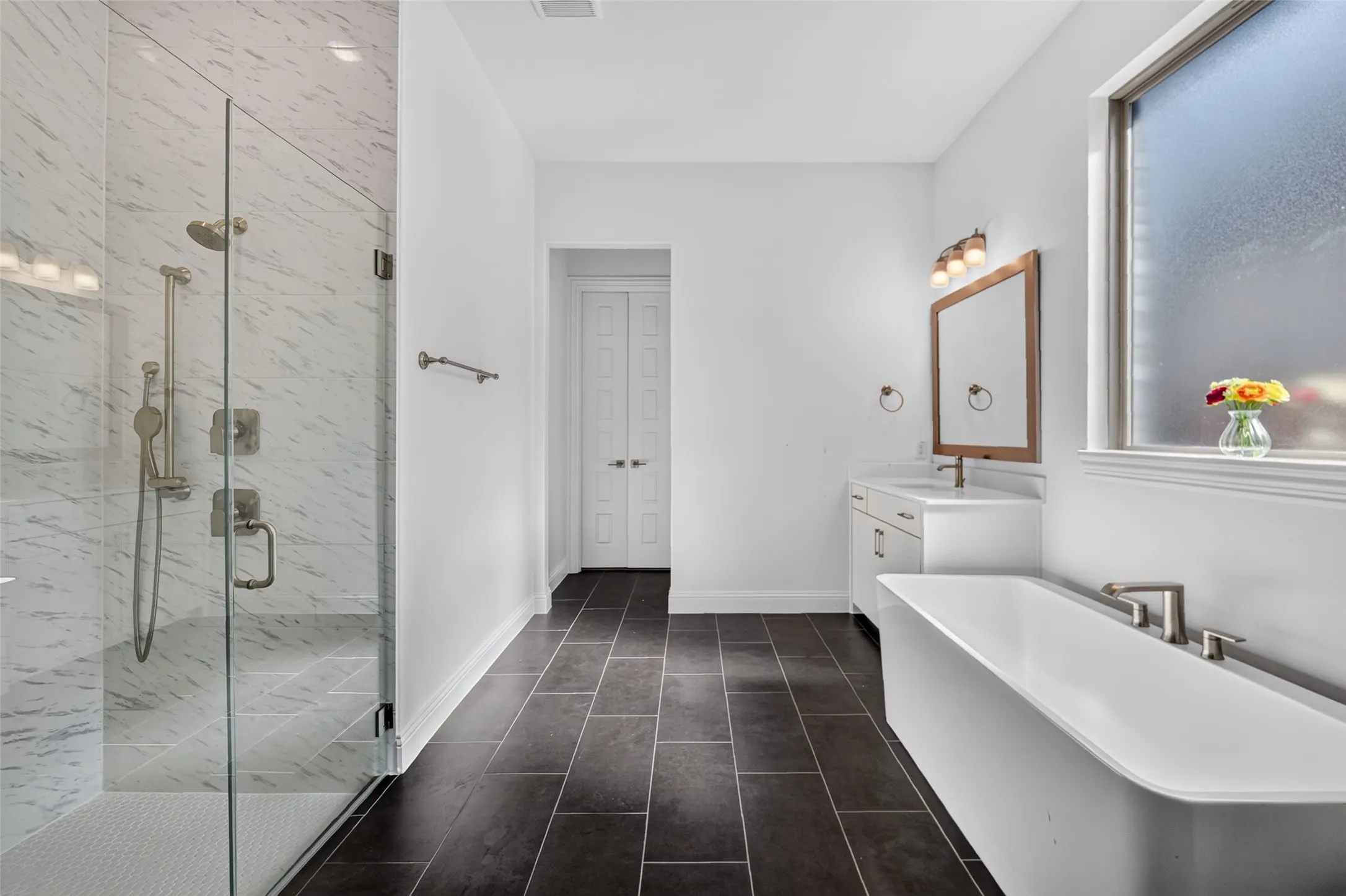 Freestanding bathtub, walk-in shower with glass enclosure, single vanity, and large-format floor tiling