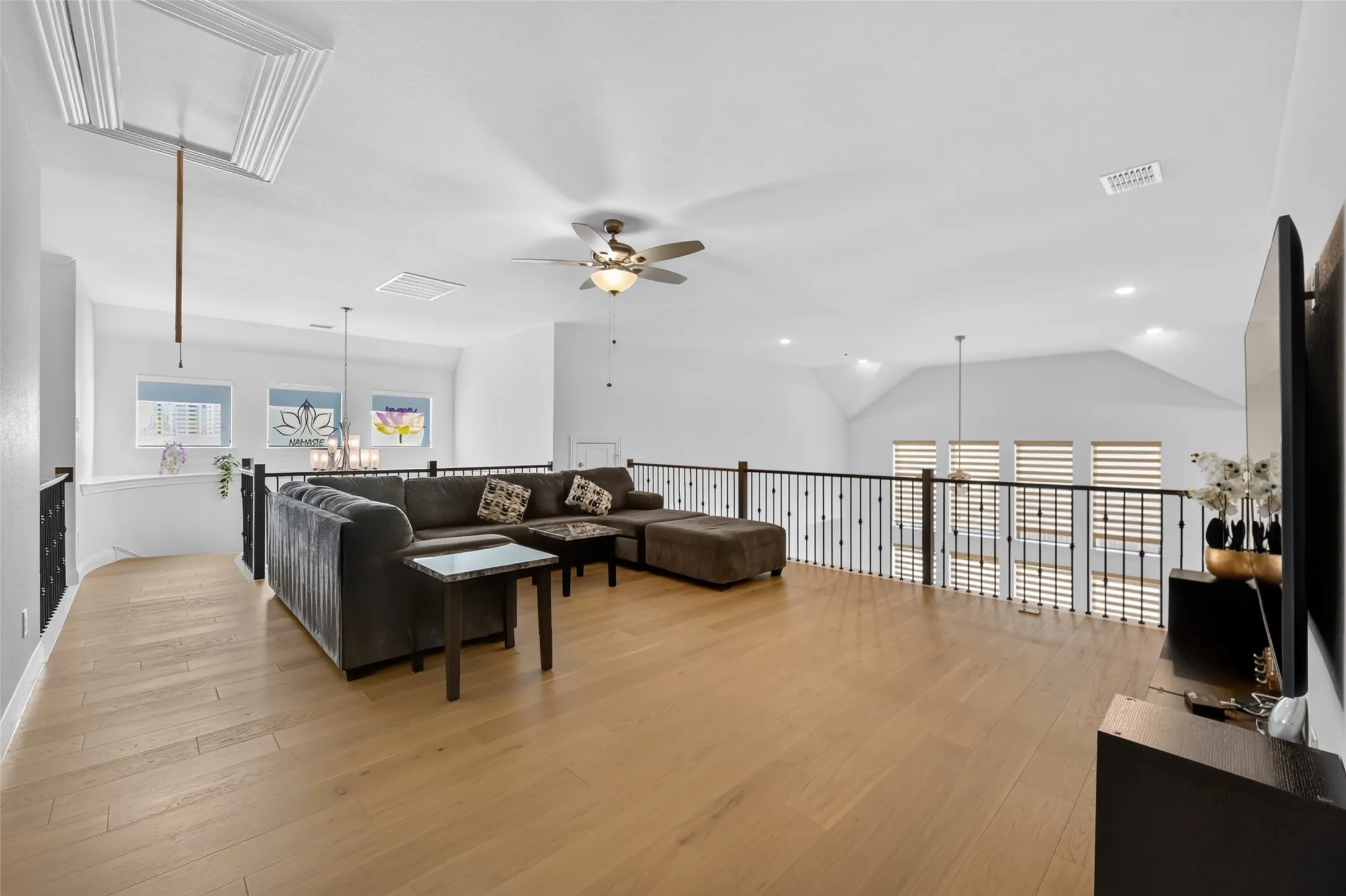Open loft area featuring wood-finish flooring, a vaulted ceiling, and a ceiling fan with integrated lighting