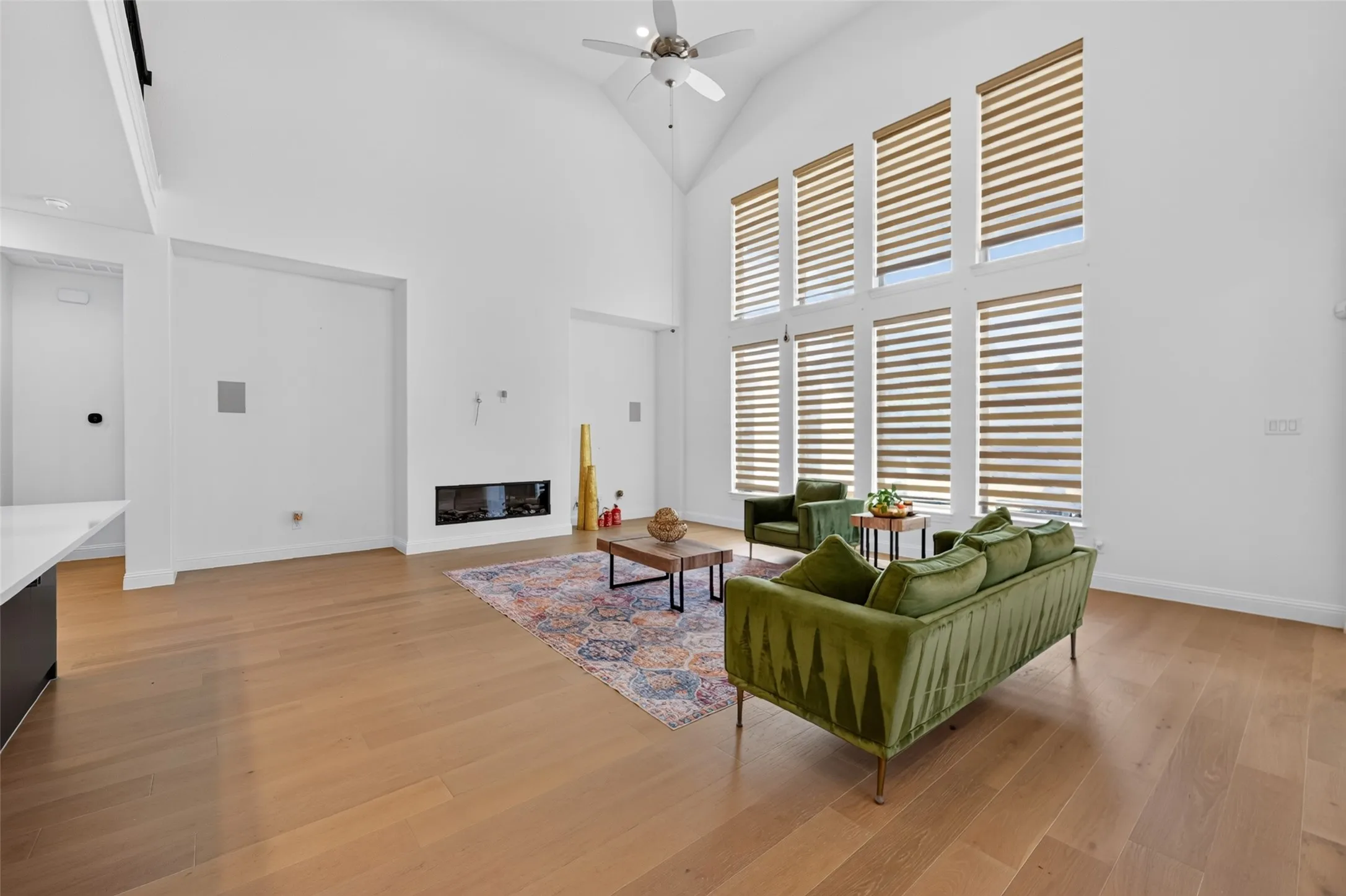 Vaulted ceiling, wood-finish flooring, full-height windows, built-in linear fireplace, and ceiling fan