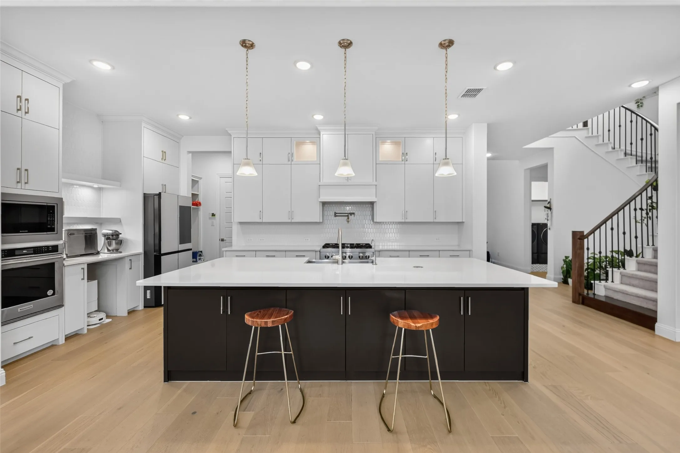 Expansive kitchen featuring a large central island, light wood-finish flooring, white cabinetry, and stainless steel appliances