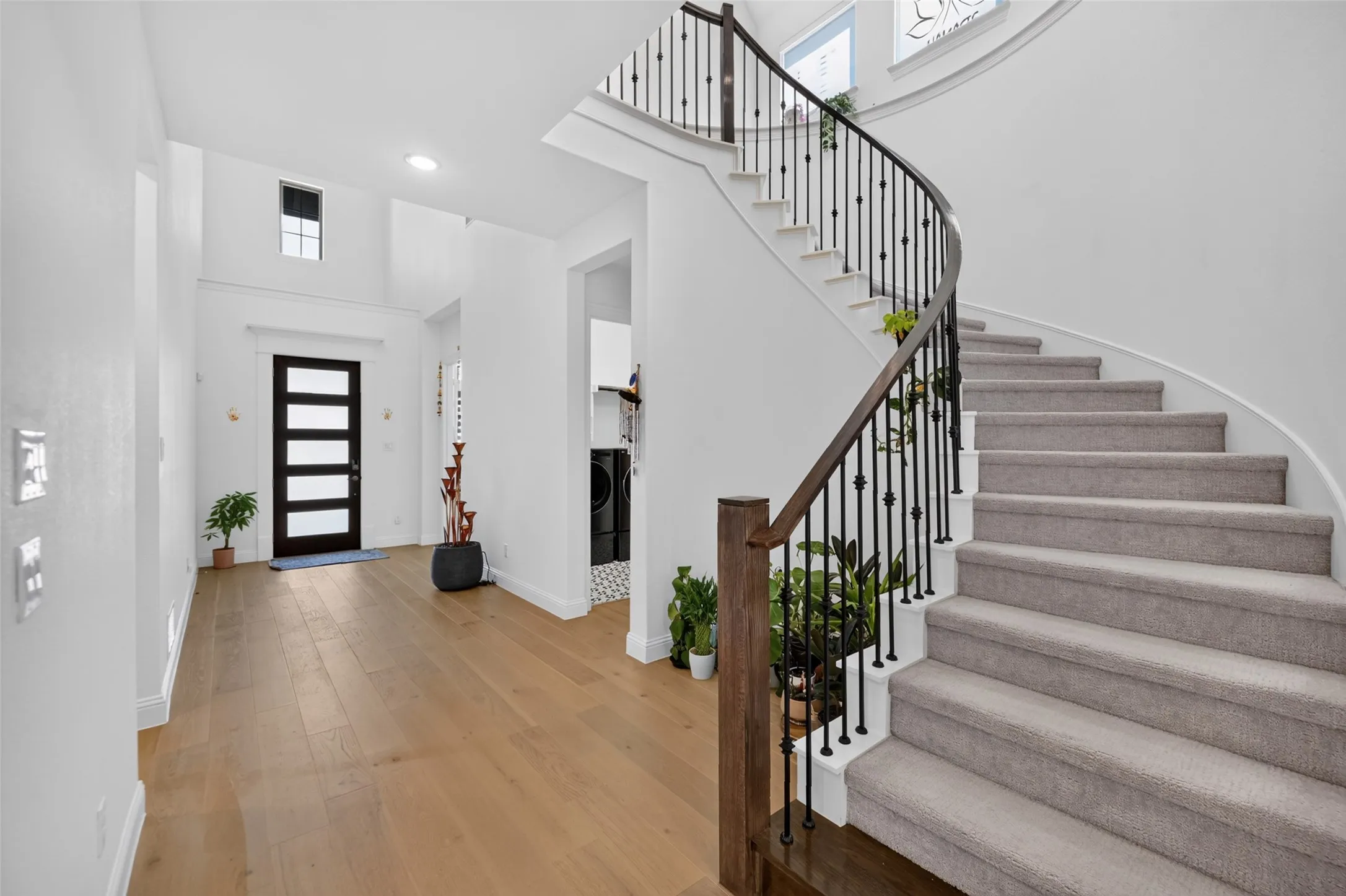Grand entrance featuring a curved staircase with wrought iron balusters and wood-finish handrail, light wood-finish flooring, and a modern front door with frosted glass panels