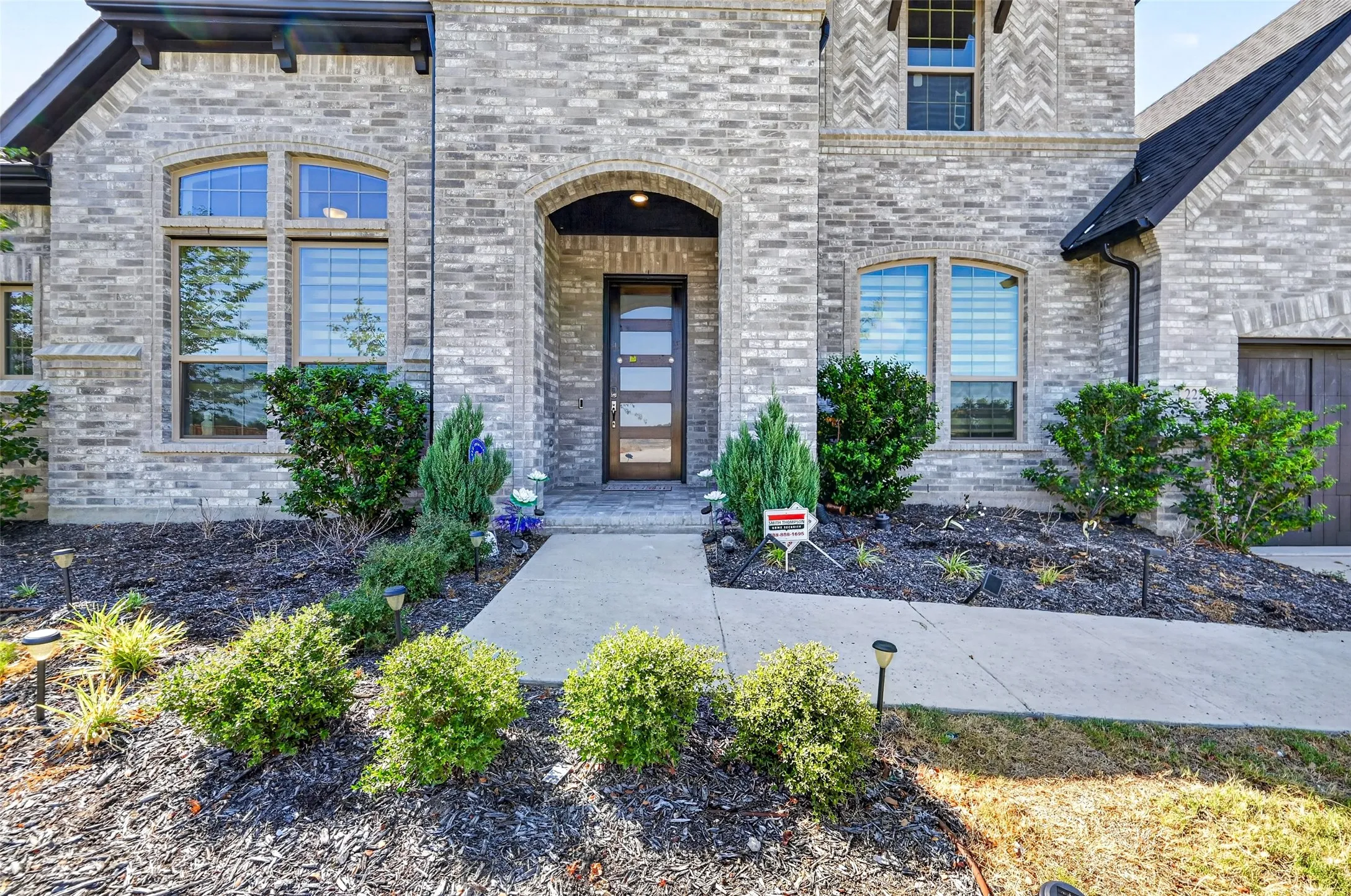Gray brick exterior with arched entryway, multi-pane windows, and a dark wood-finish door with frosted glass inserts