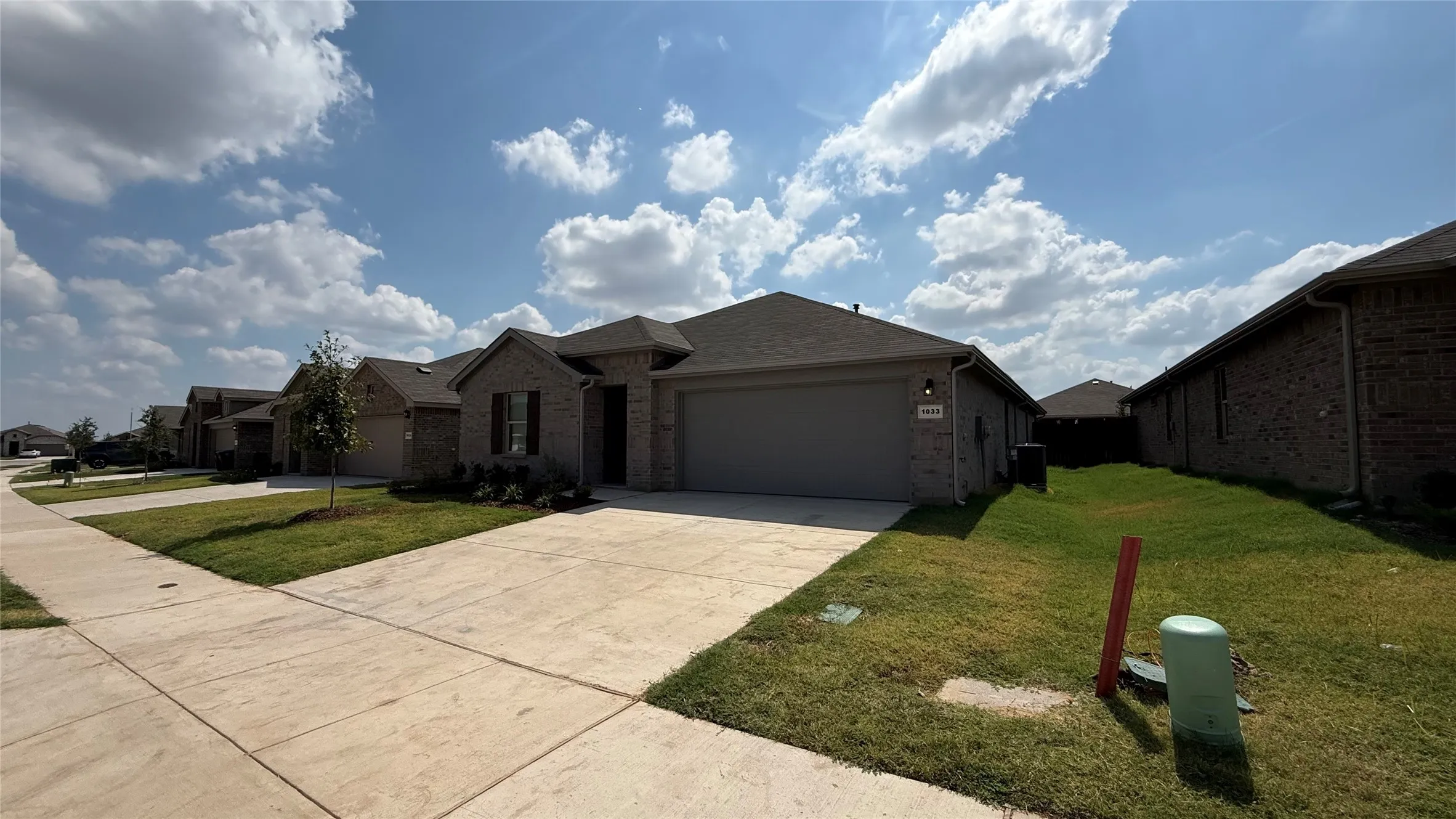 Brick exterior residence featuring a two-car garage, concrete driveway, and established landscaping