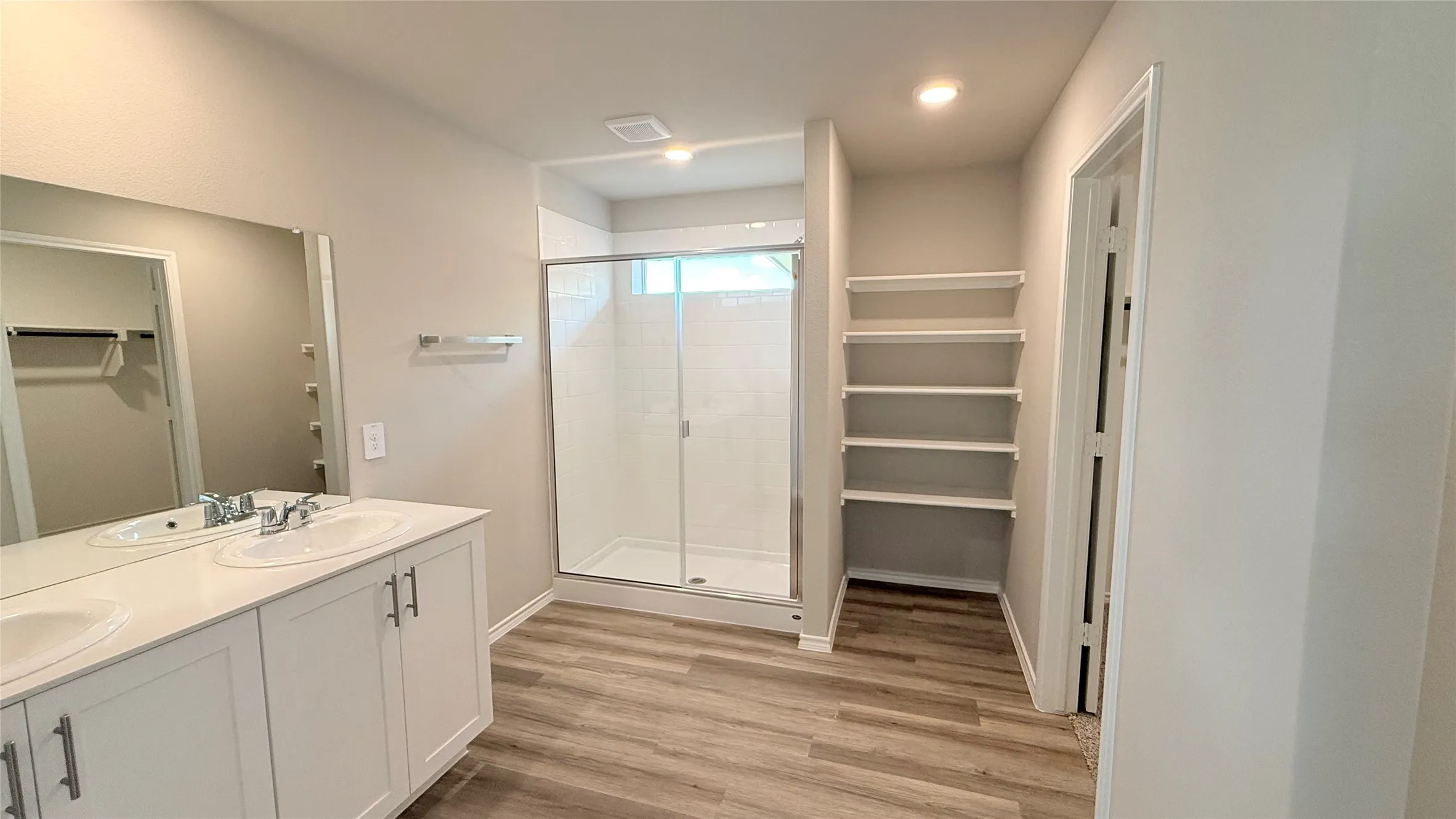 Dual vanity with white cabinetry, glass-enclosed shower, wood-finish flooring, recessed lighting, and built-in shelving