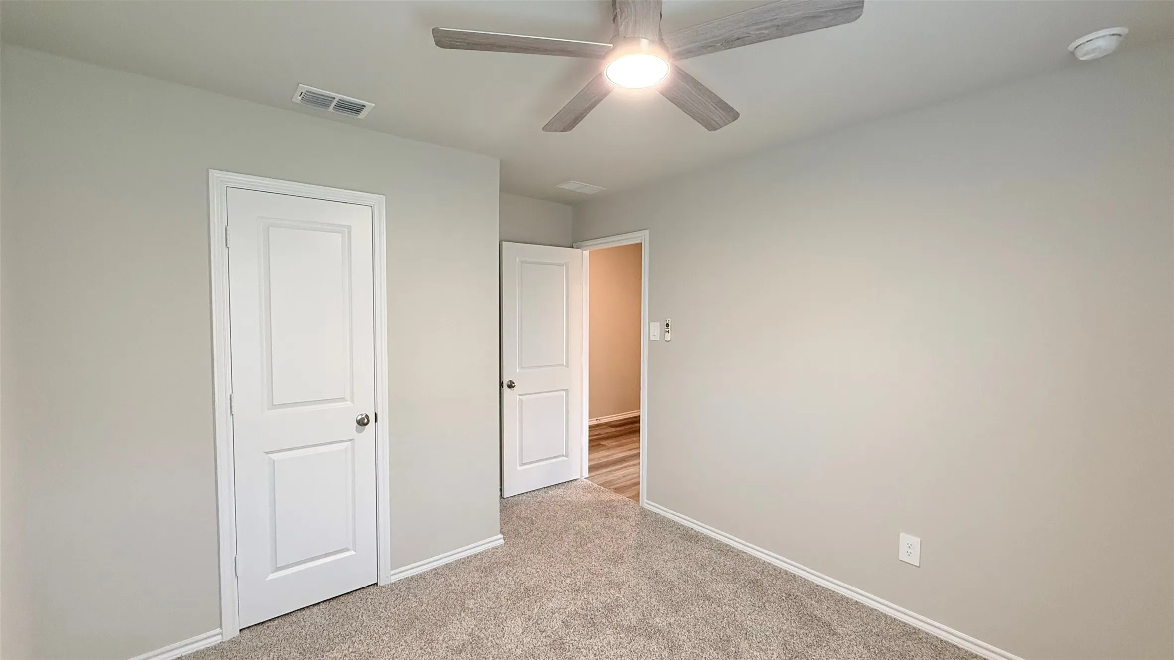 Light gray wall paint, neutral-toned carpeting, white two-panel interior doors, and a ceiling fan with integrated lighting